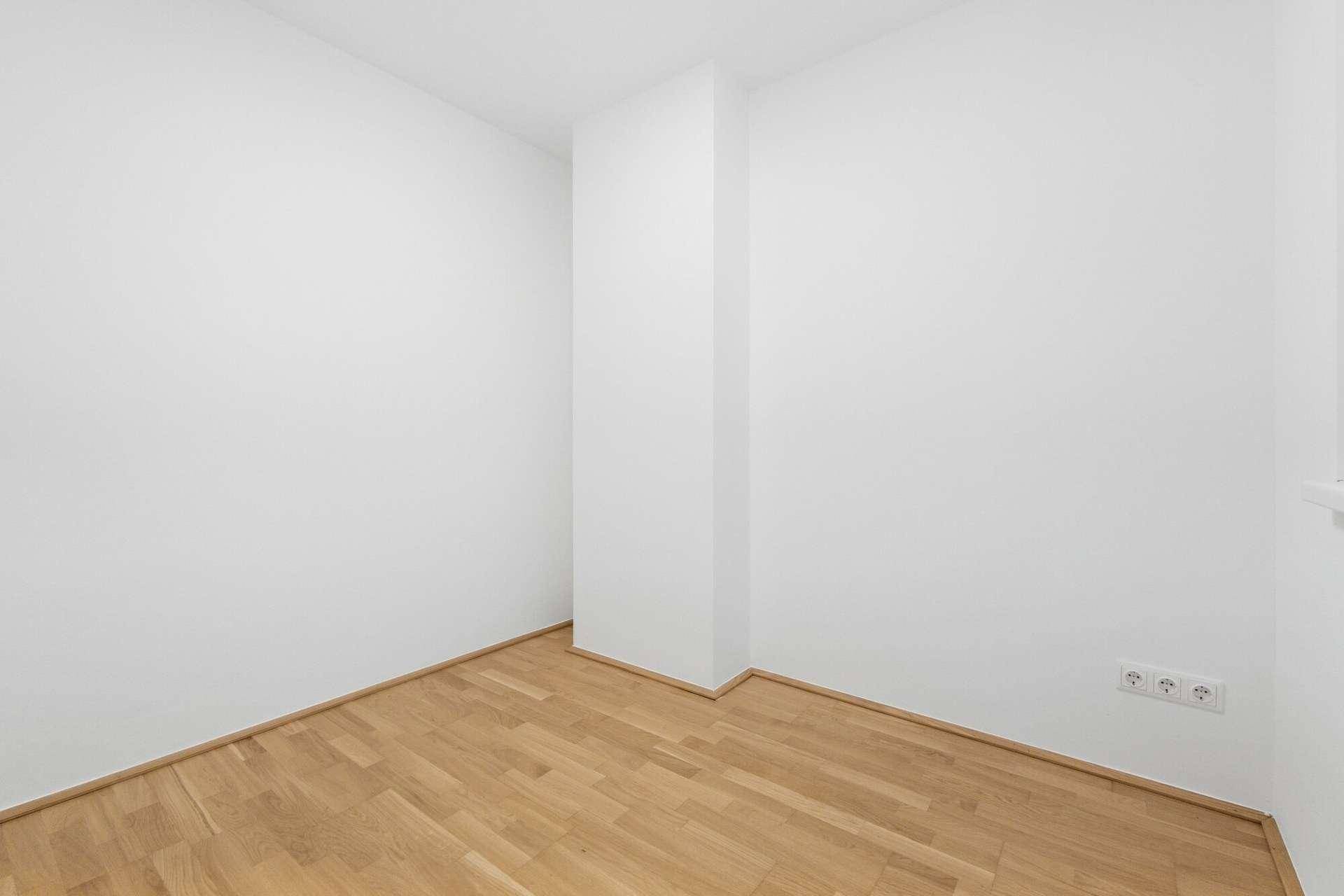 Leeres Zimmer mit hellem Parkettboden und weißen Wänden, bereit zur individuellen Gestaltung.