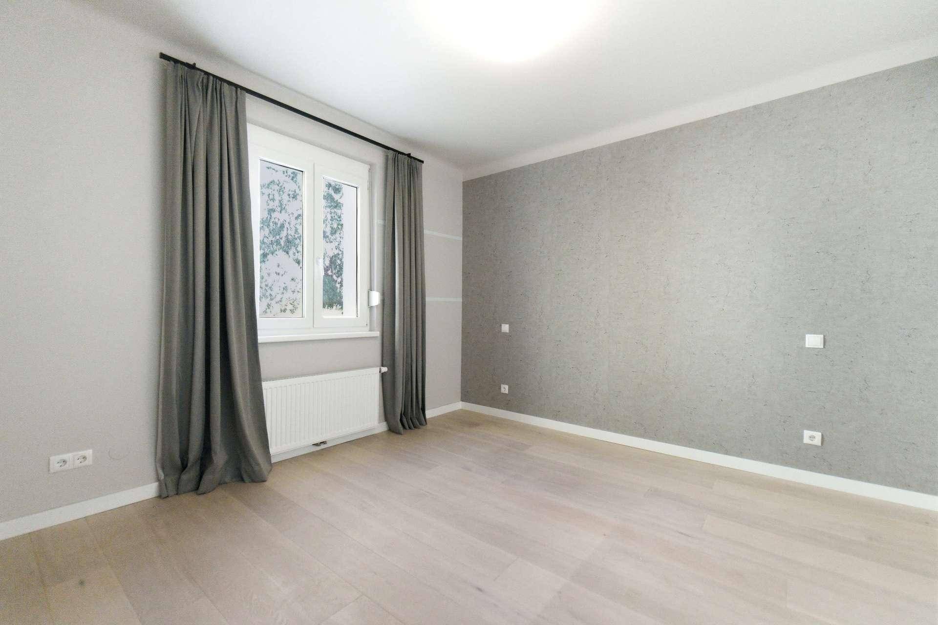 Geräumiges Schlafzimmer mit hellem Boden, grauer Akzentwand und Vorhängen.