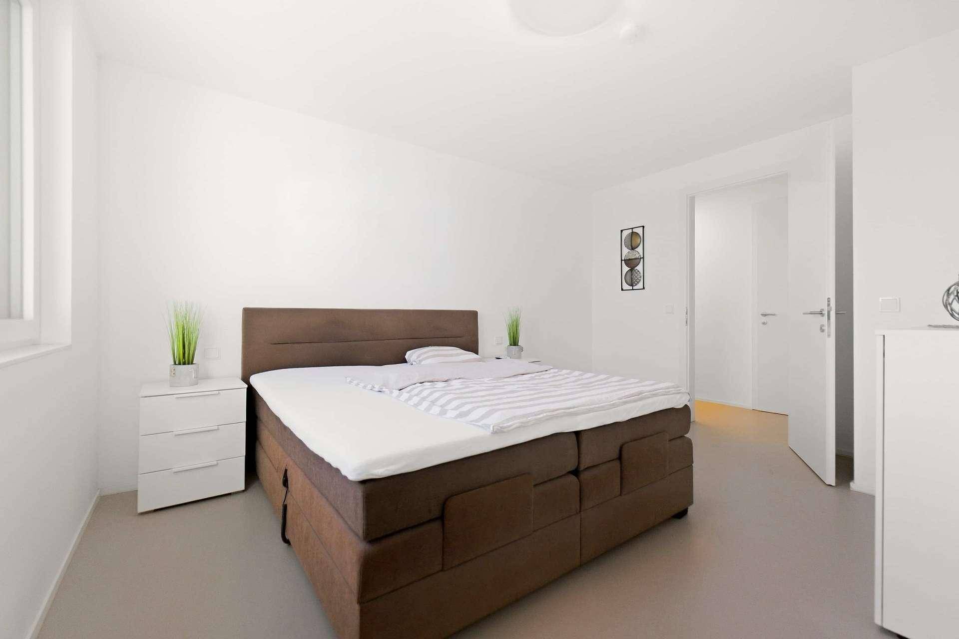 Helles Schlafzimmer mit großem Boxspringbett, Nachttischen und minimalistischer Einrichtung.