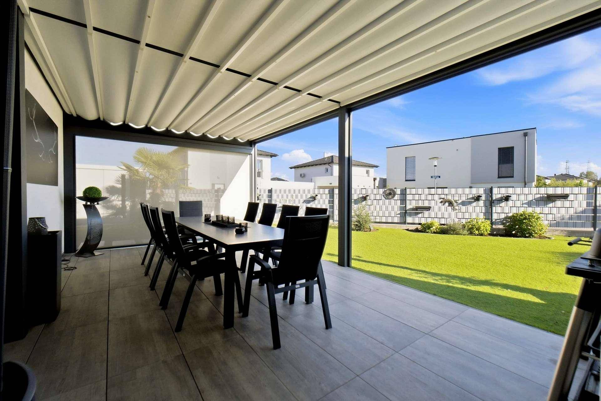 Geräumige überdachte Terrasse mit Esstisch und Blick auf den grünen Garten.
