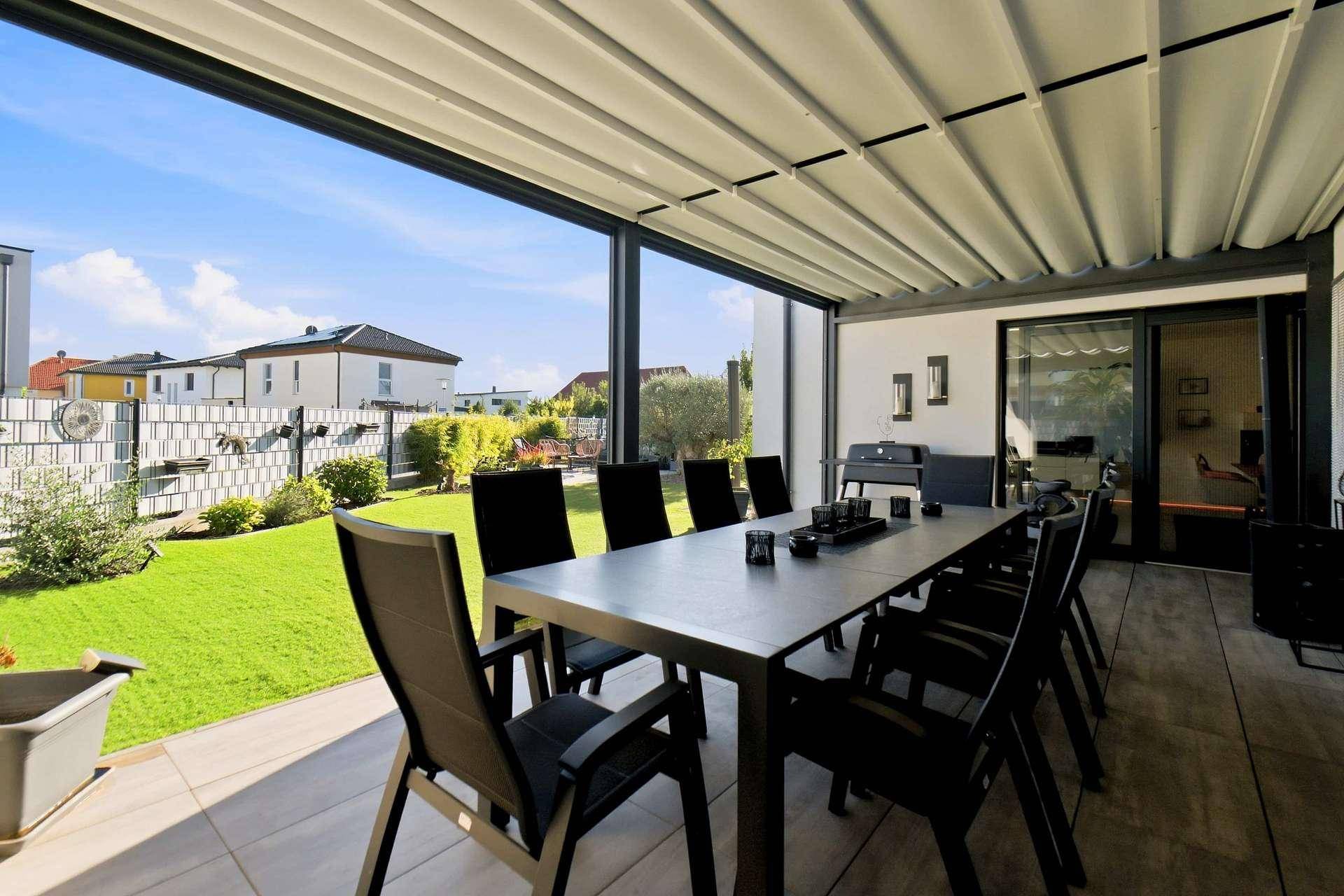 Überdachte Terrasse mit großem Esstisch und Blick auf den gepflegten Garten.