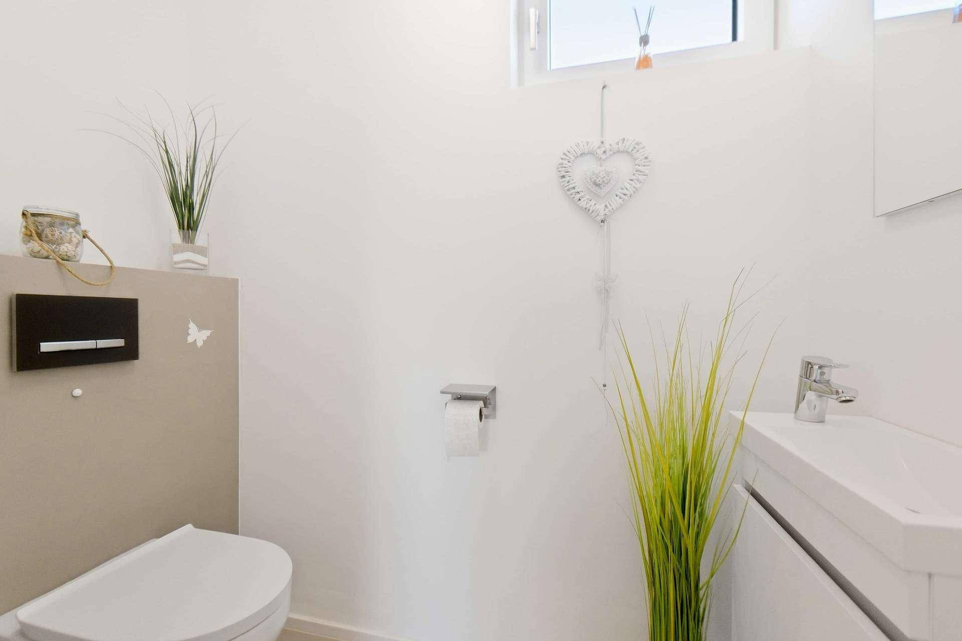 Sauberes Gäste-WC mit wandhängender Toilette, kleinem Waschbecken und schlichter Dekoration.