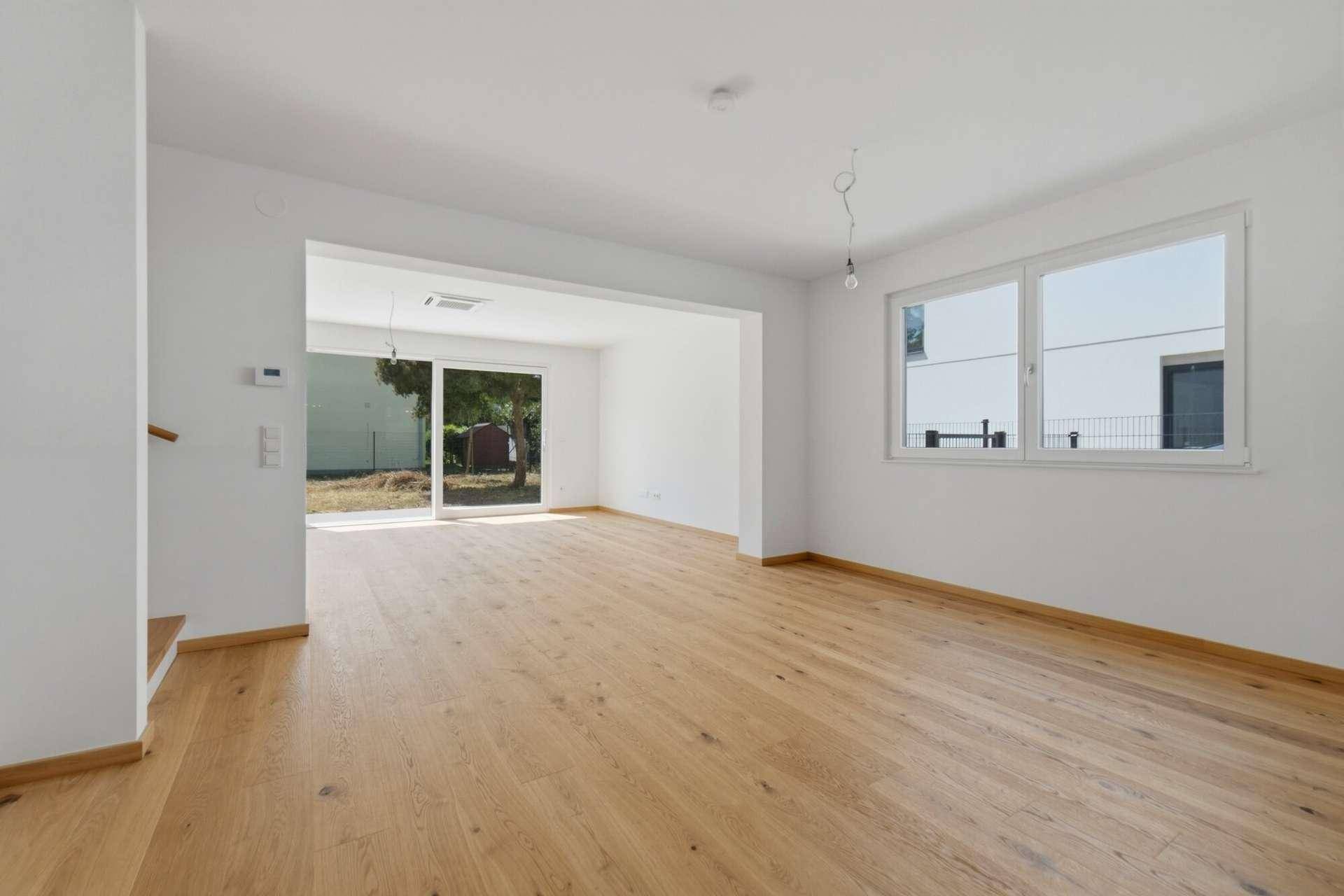 Geräumiges Wohnzimmer mit Holzboden, großen Fenstern und Blick ins Grüne.