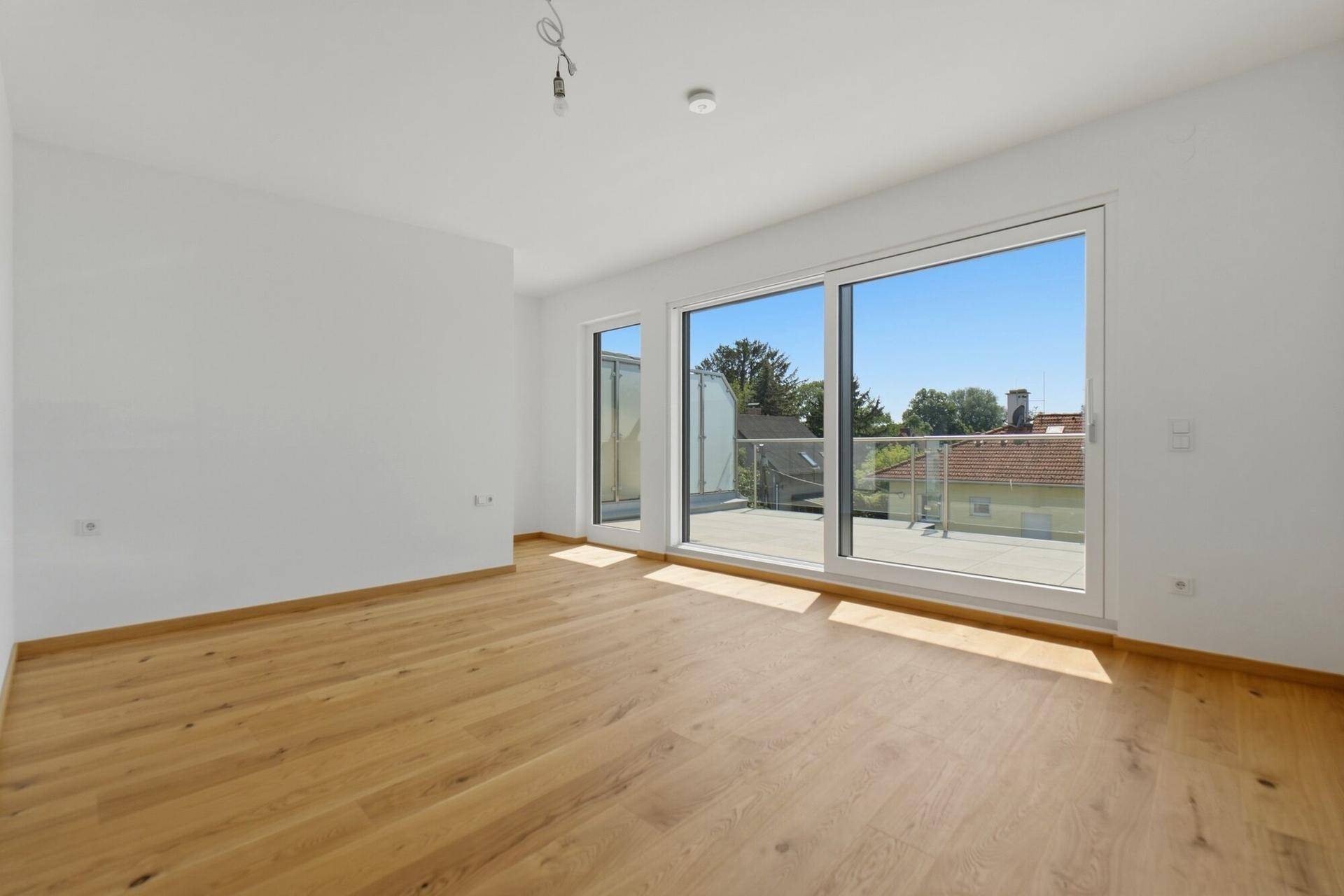 Geräumiges, leeres Zimmer mit Eichenparkett und großen Schiebetüren zur Terrasse.