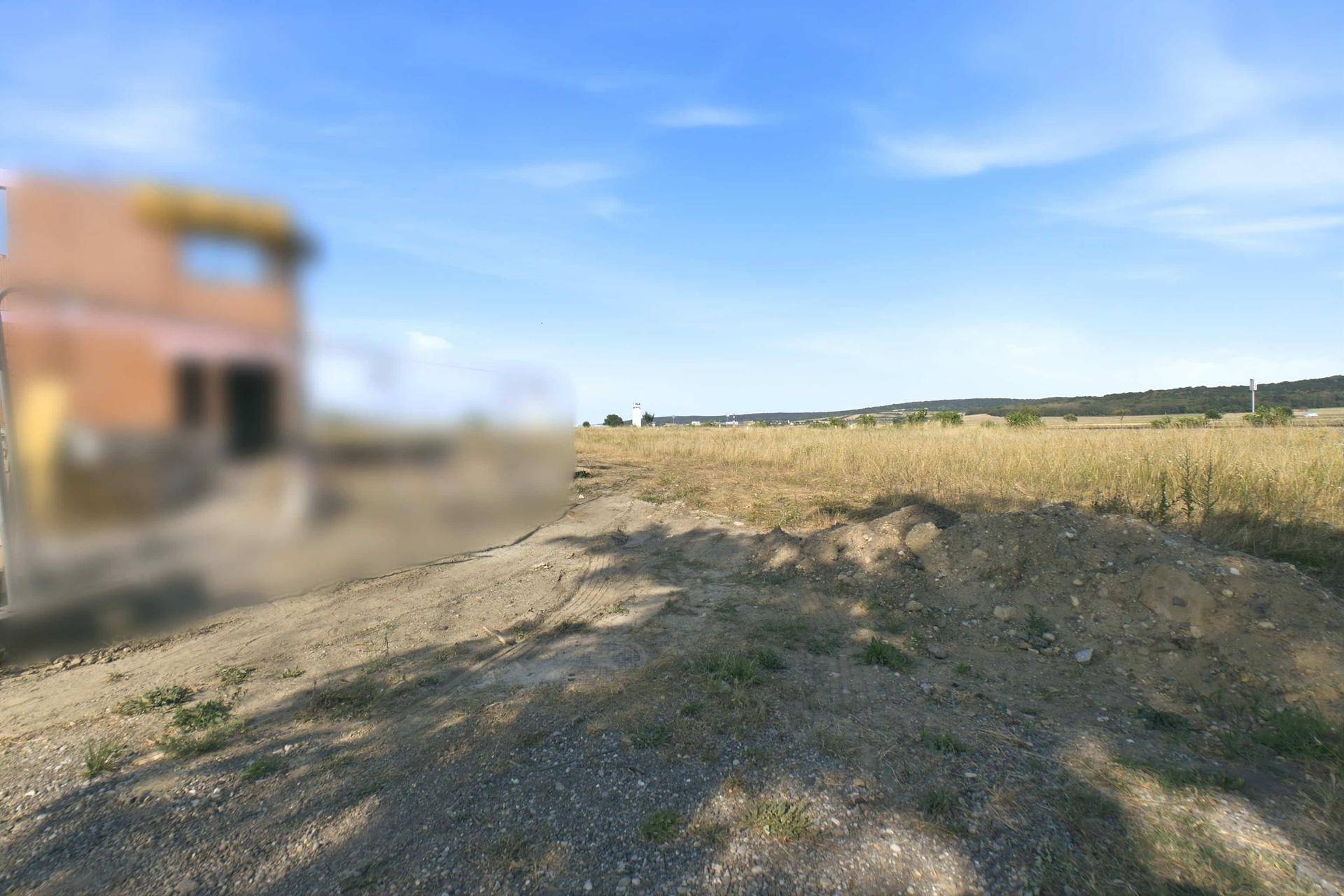 Weites, trockenes Feld unter blauem Himmel mit einer verschwommenen Baustelle am linken Bildrand.