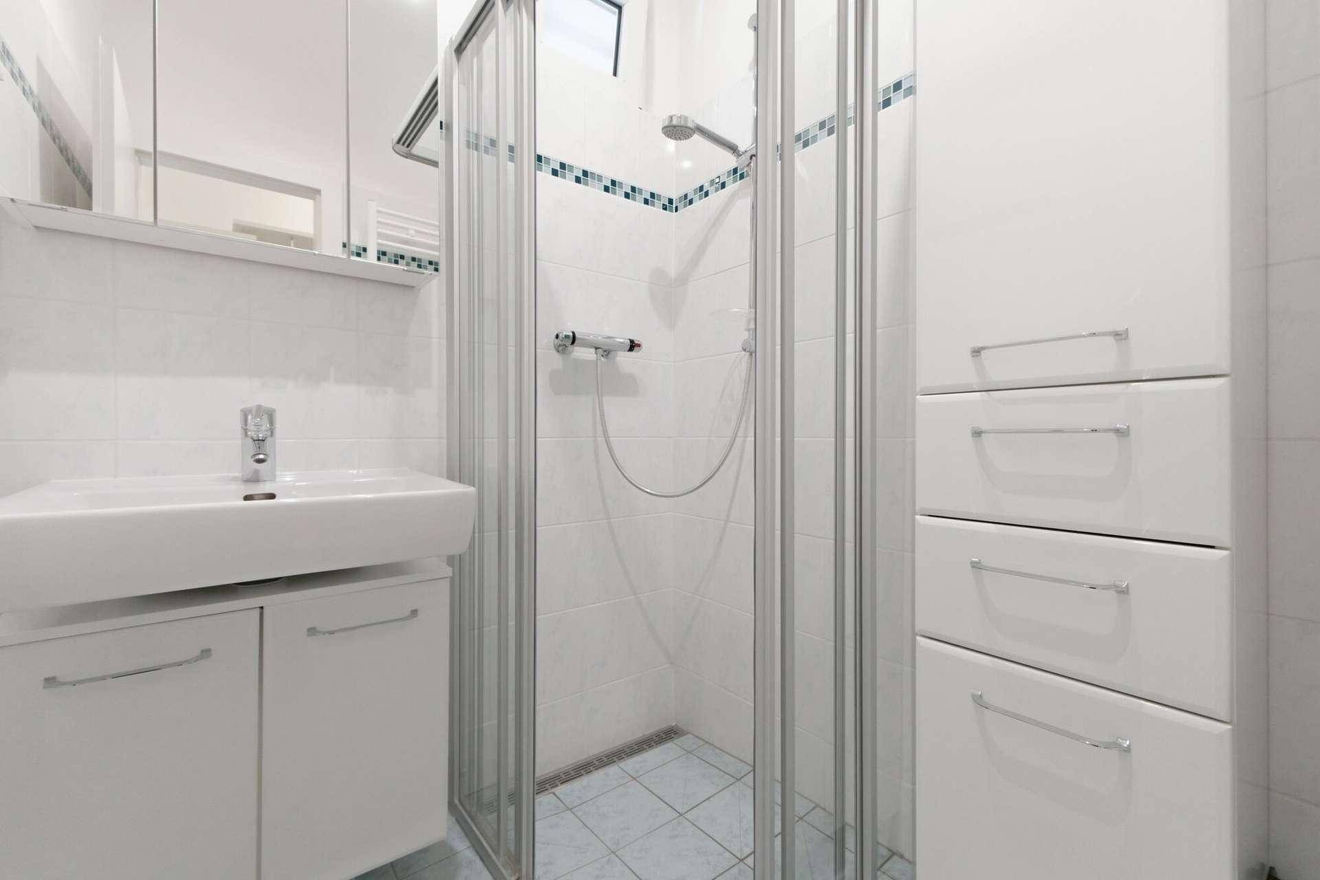 Helles Badezimmer mit Duschkabine, Waschbecken und weißen Fliesen mit blauen Akzenten.