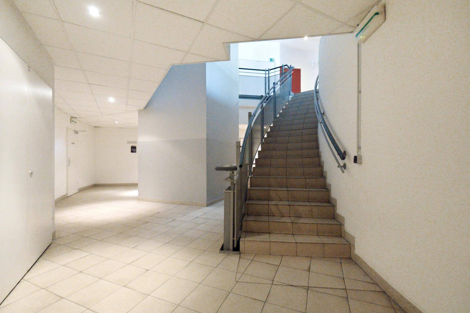 Geräumiger Flur mit Treppenhaus, Fliesenboden und hellen Wänden in einem Mehrfamilienhaus.