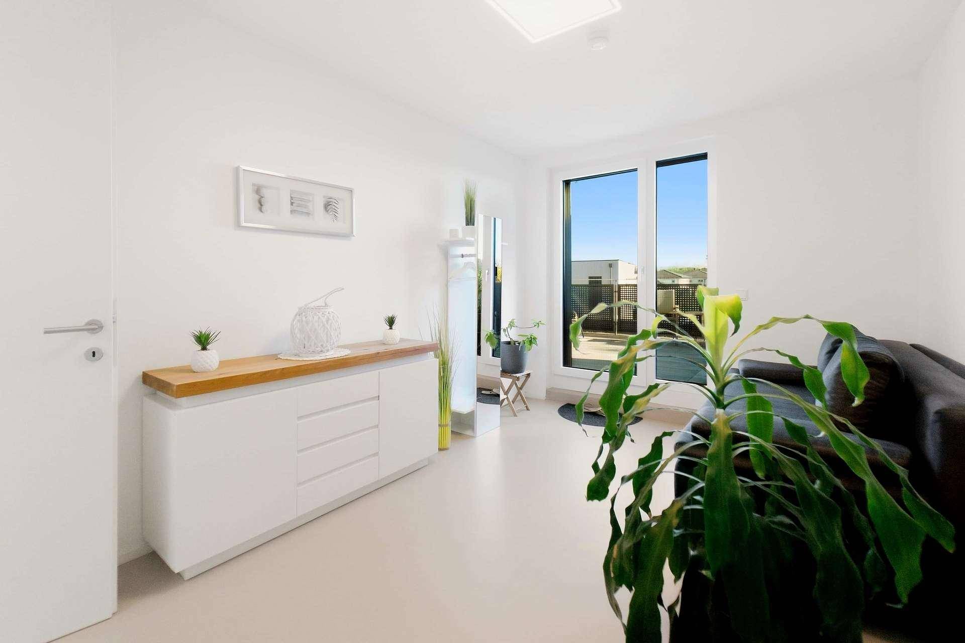Modern eingerichtetes Wohnzimmer mit weißem Sideboard und großem Fenster.