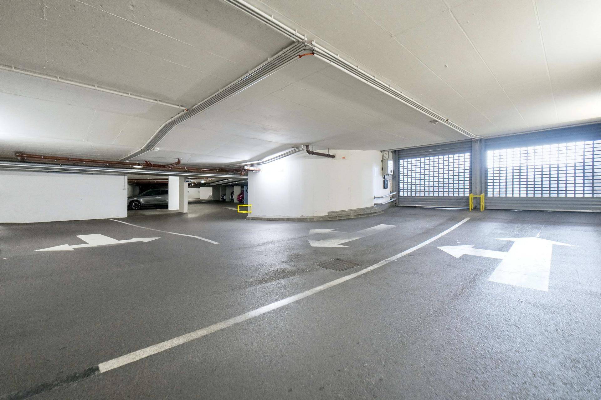 Innenansicht einer Tiefgarage mit Fahrbahnmarkierungen, einer Kurve und einem Rolltor.
