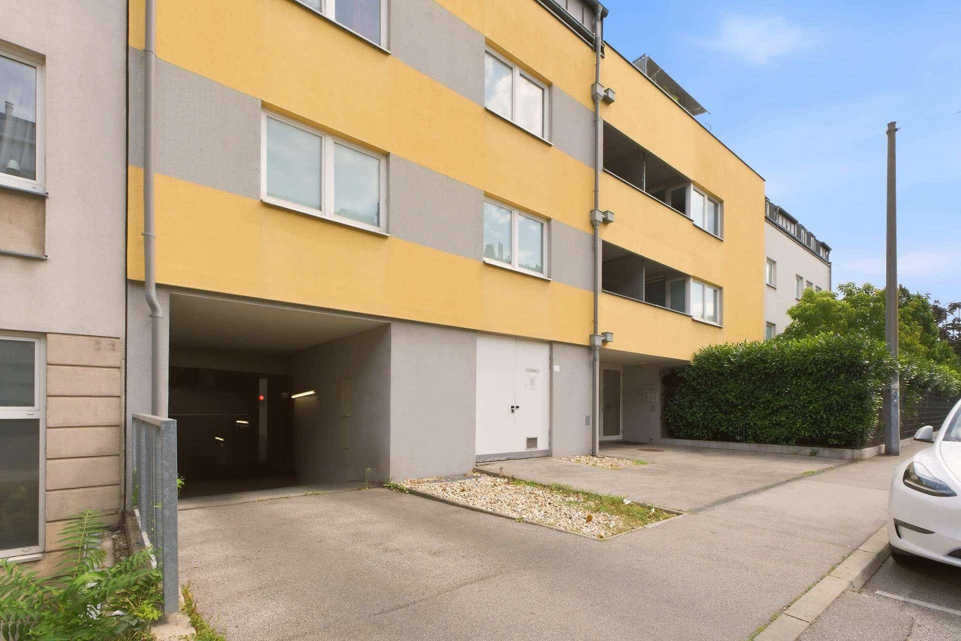 Moderne Gebäudefassade in Gelb und Grau mit Zufahrt zur Tiefgarage.