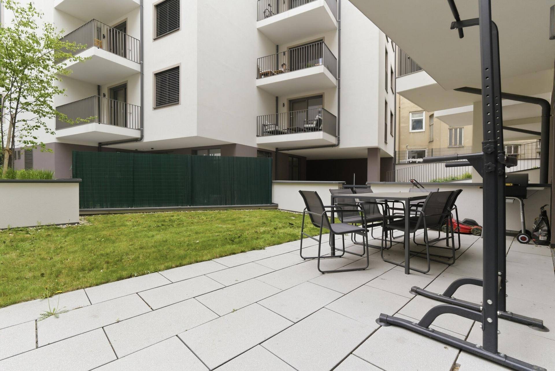 Außenbereich mit gepflasterter Terrasse, Gartenmöbeln und Rasenfläche in einer Wohnanlage.