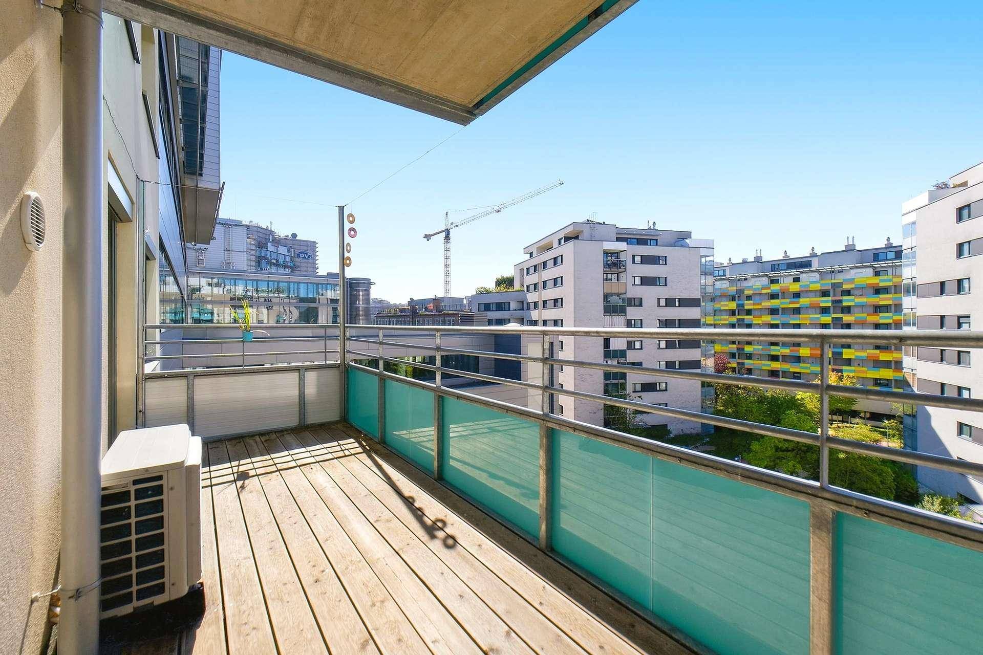 Sonniger Balkon mit Holzboden und Blick auf moderne Wohngebäude in der Stadt.