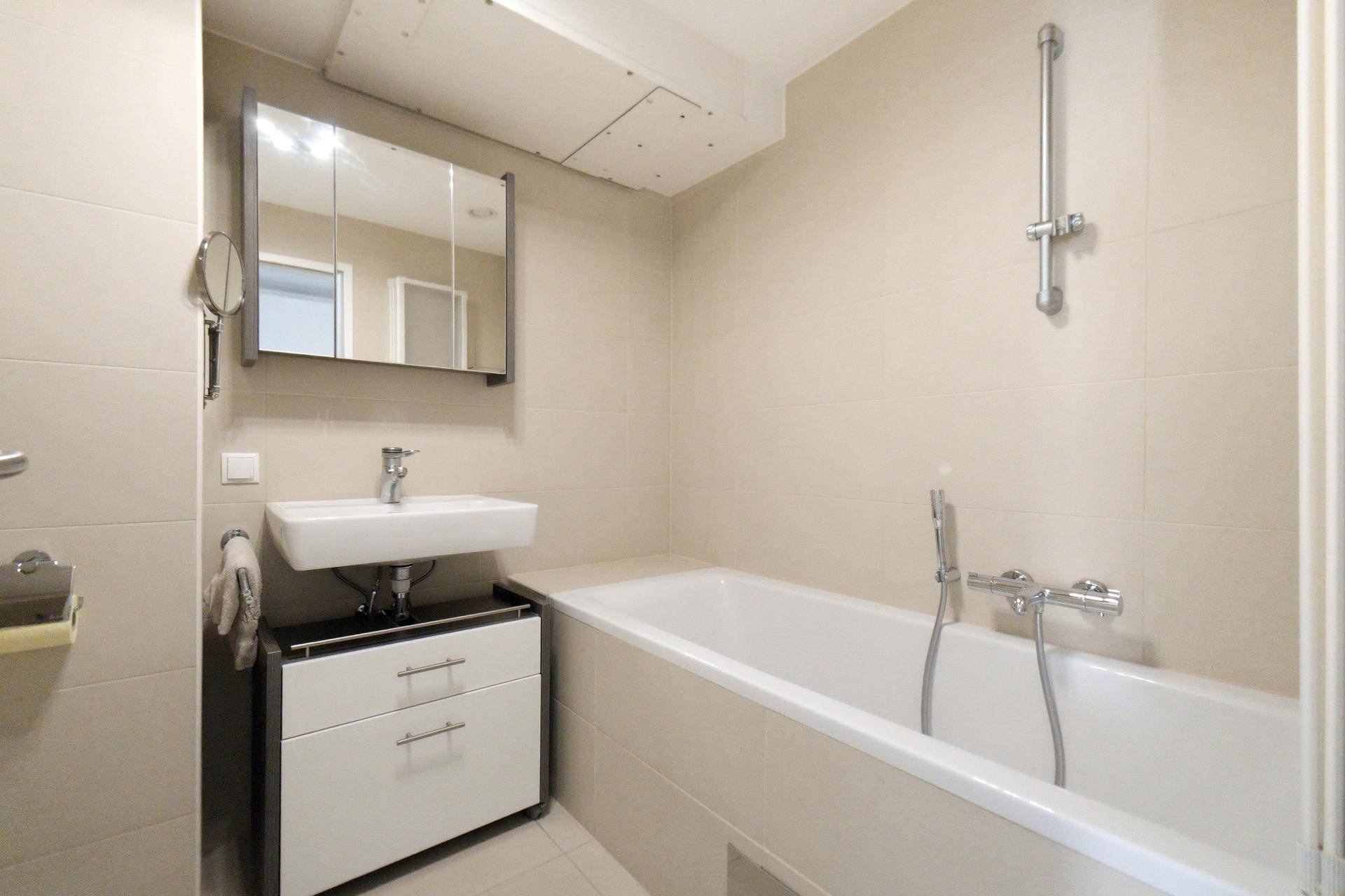 Helles Badezimmer mit Badewanne, Waschbecken und Spiegelschrank, ausgestattet mit beigen Fliesen.