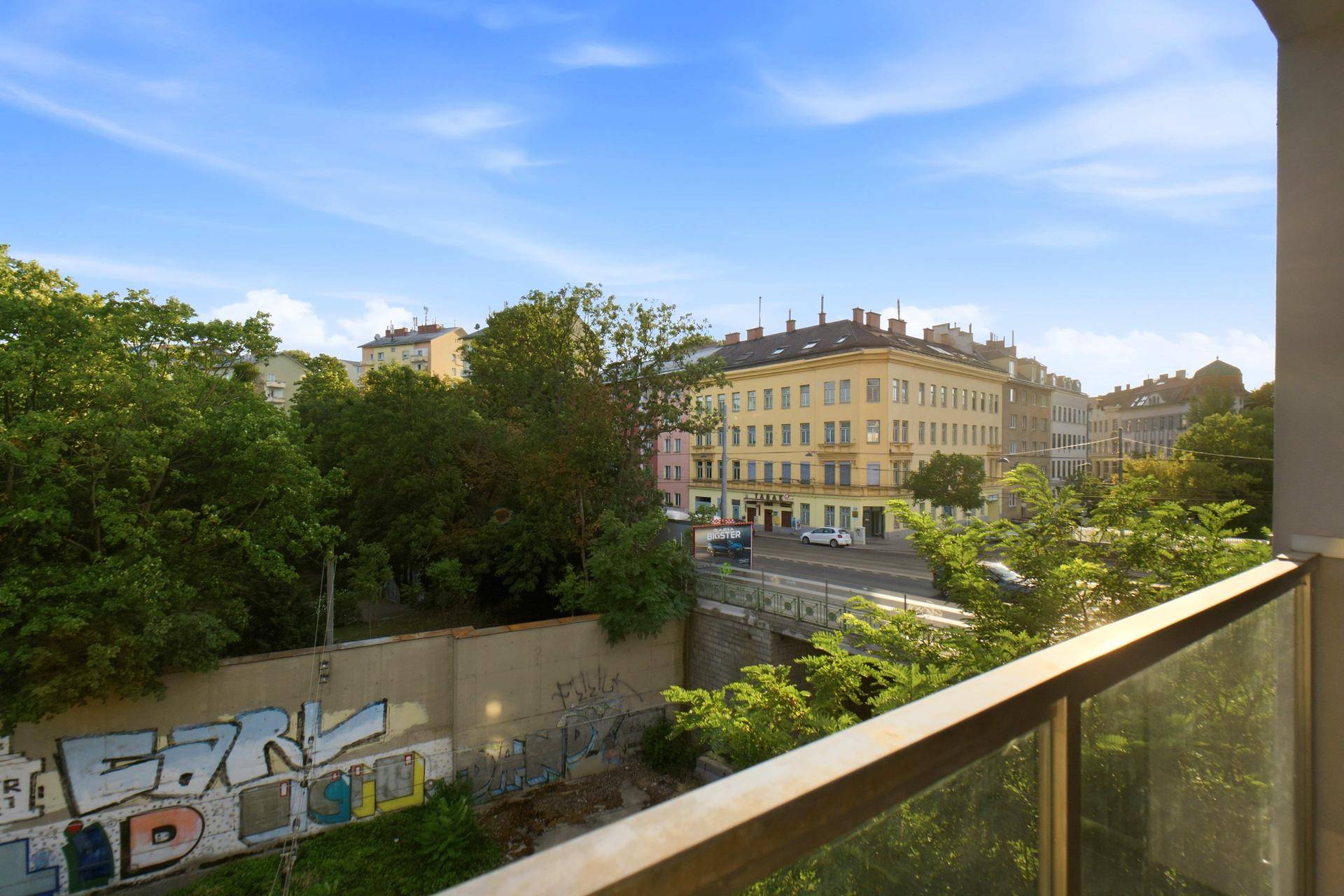 Balkonblick auf eine städtische Umgebung mit Gebäuden, Bäumen und einer Straße.