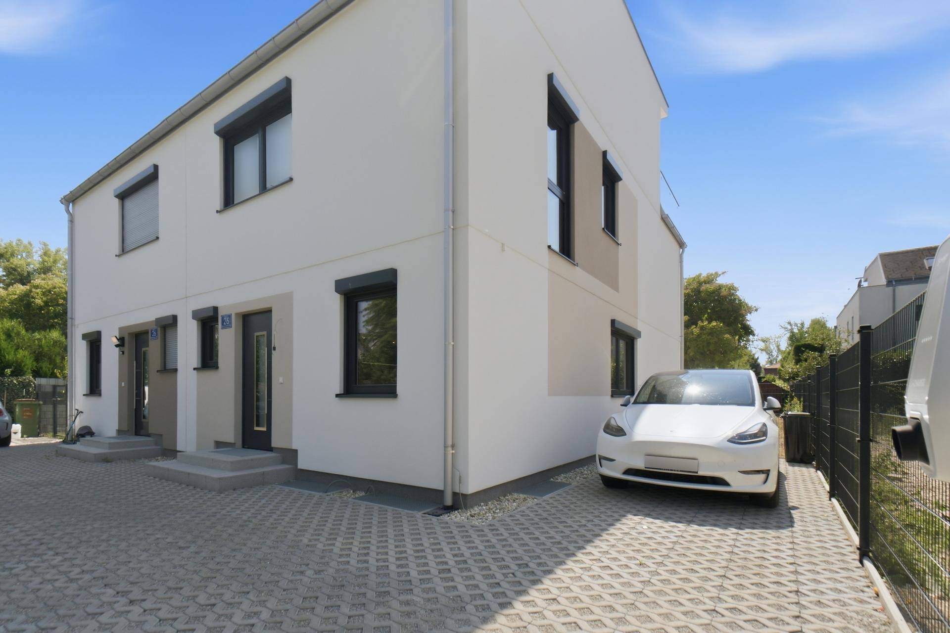 Vorderansicht einer modernen Doppelhaushälfte mit gepflasterter Einfahrt und Parkplatz.