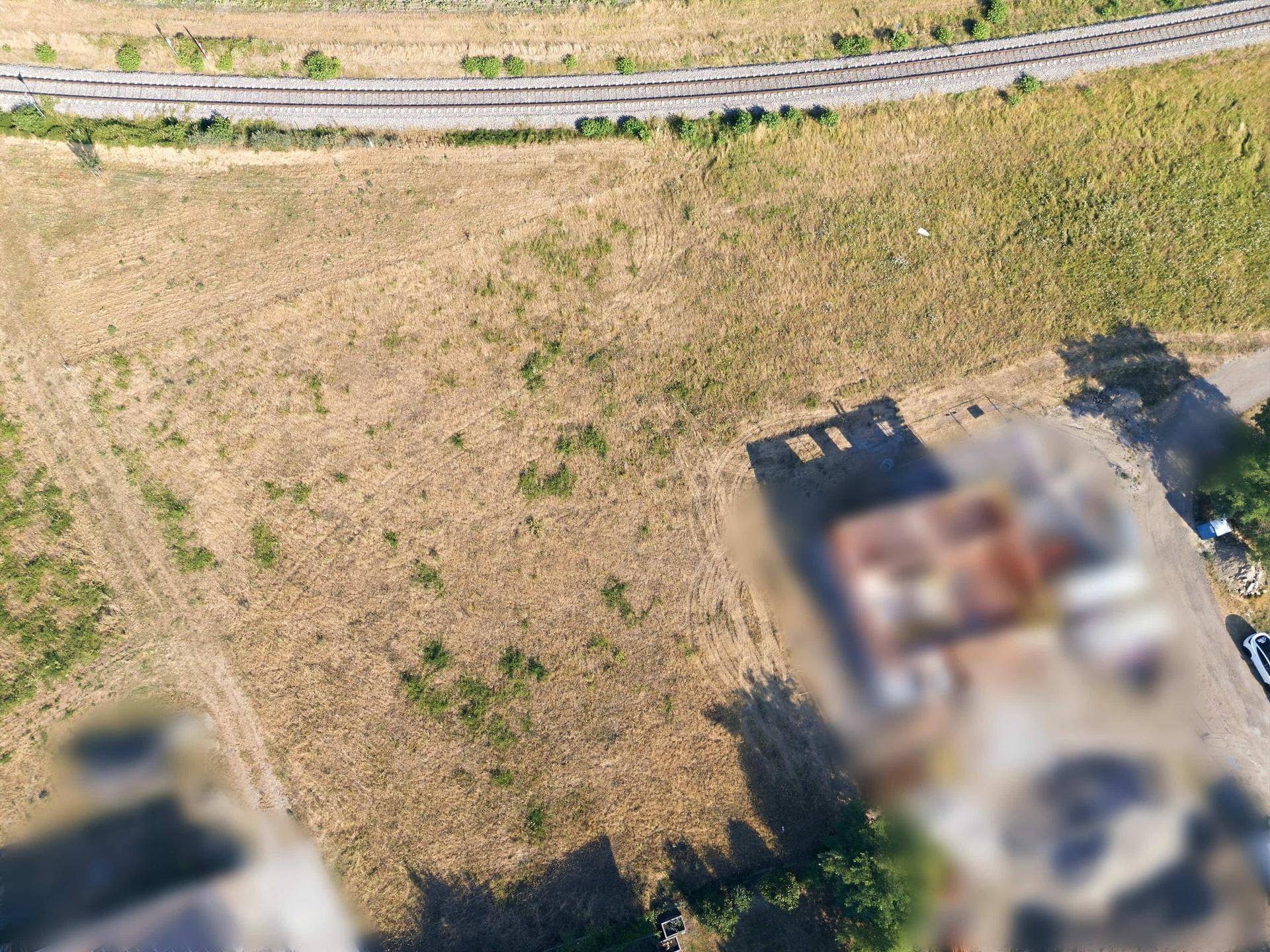 Blick von oben auf ein trockenes Feld, angrenzende Bahngleise und eine Baustelle in der Ferne.