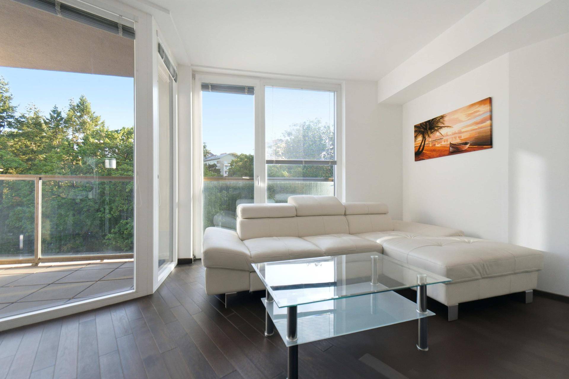 Helles Wohnzimmer mit weißem Sofa, dunklem Holzboden und großen Fenstern mit Grünblick.
