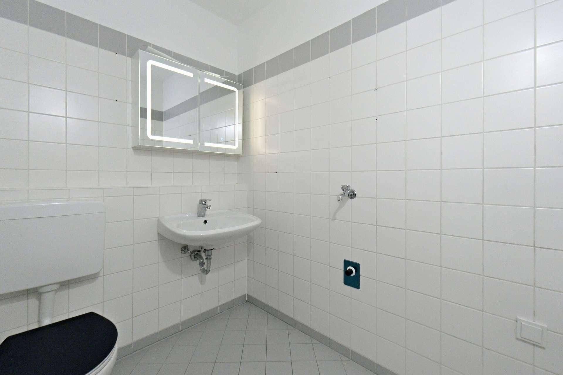 Modernes Badezimmer mit weißen Fliesen, WC, Waschbecken und beleuchtetem Spiegelschrank.