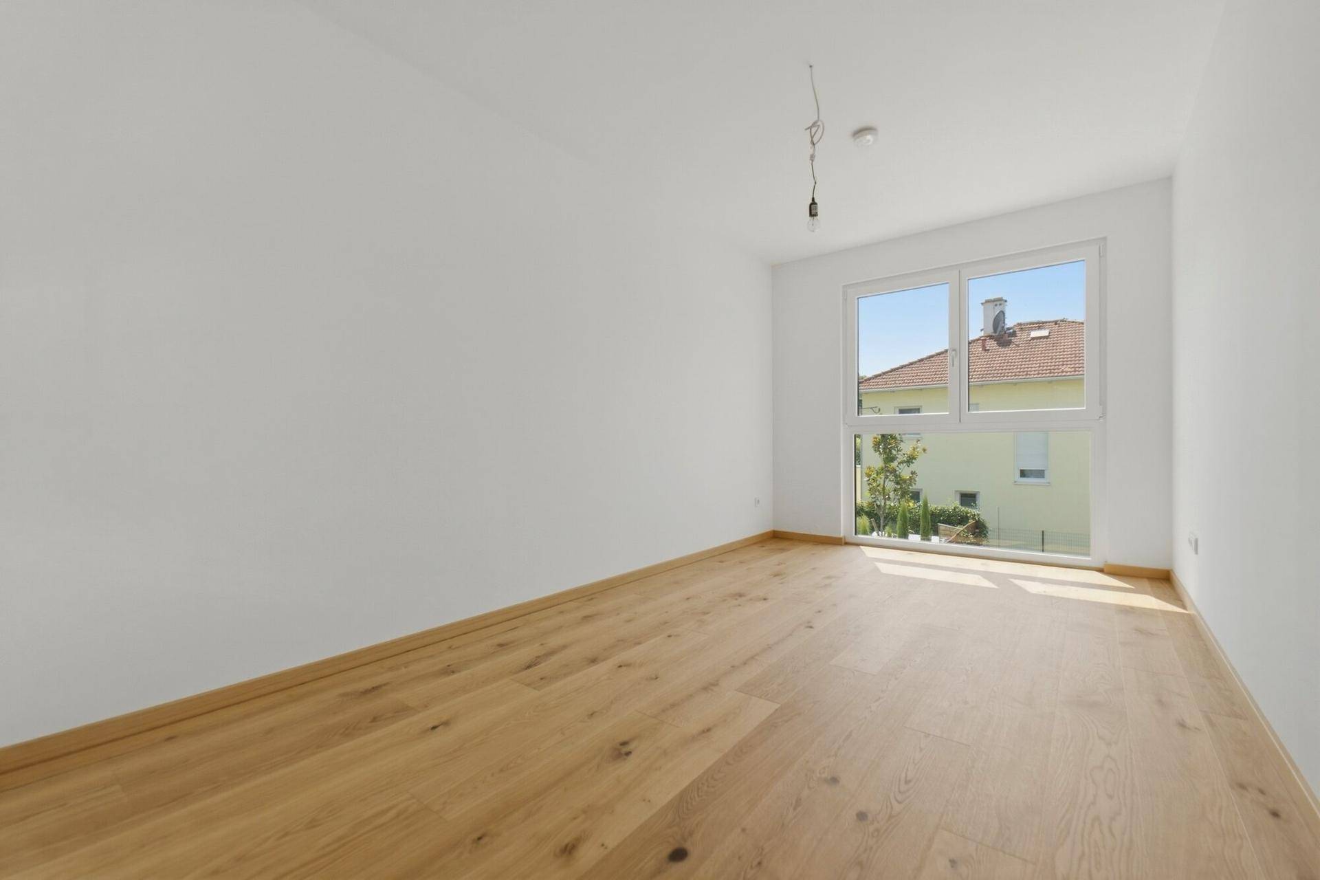 Lichtdurchflutetes Schlafzimmer mit Holzboden und weitem Ausblick durch das große Fenster.