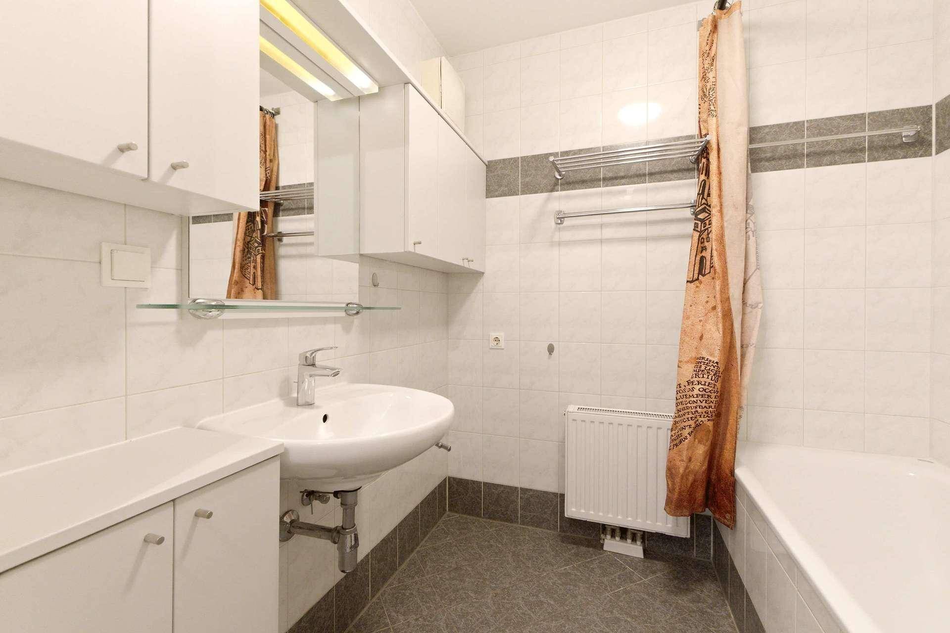 Badezimmer mit Waschbecken, Spiegelschrank, Badewanne und hellen Fliesen an Wänden und Boden.
