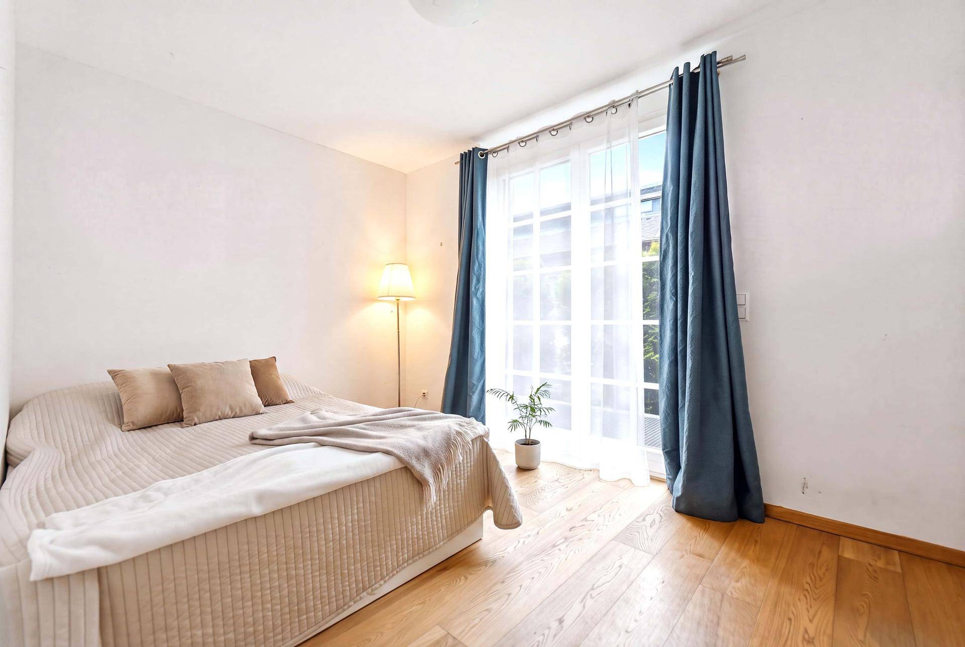 Helles Schlafzimmer mit Holzboden, großem Fenster und blauen Vorhängen, einladend eingerichtet.