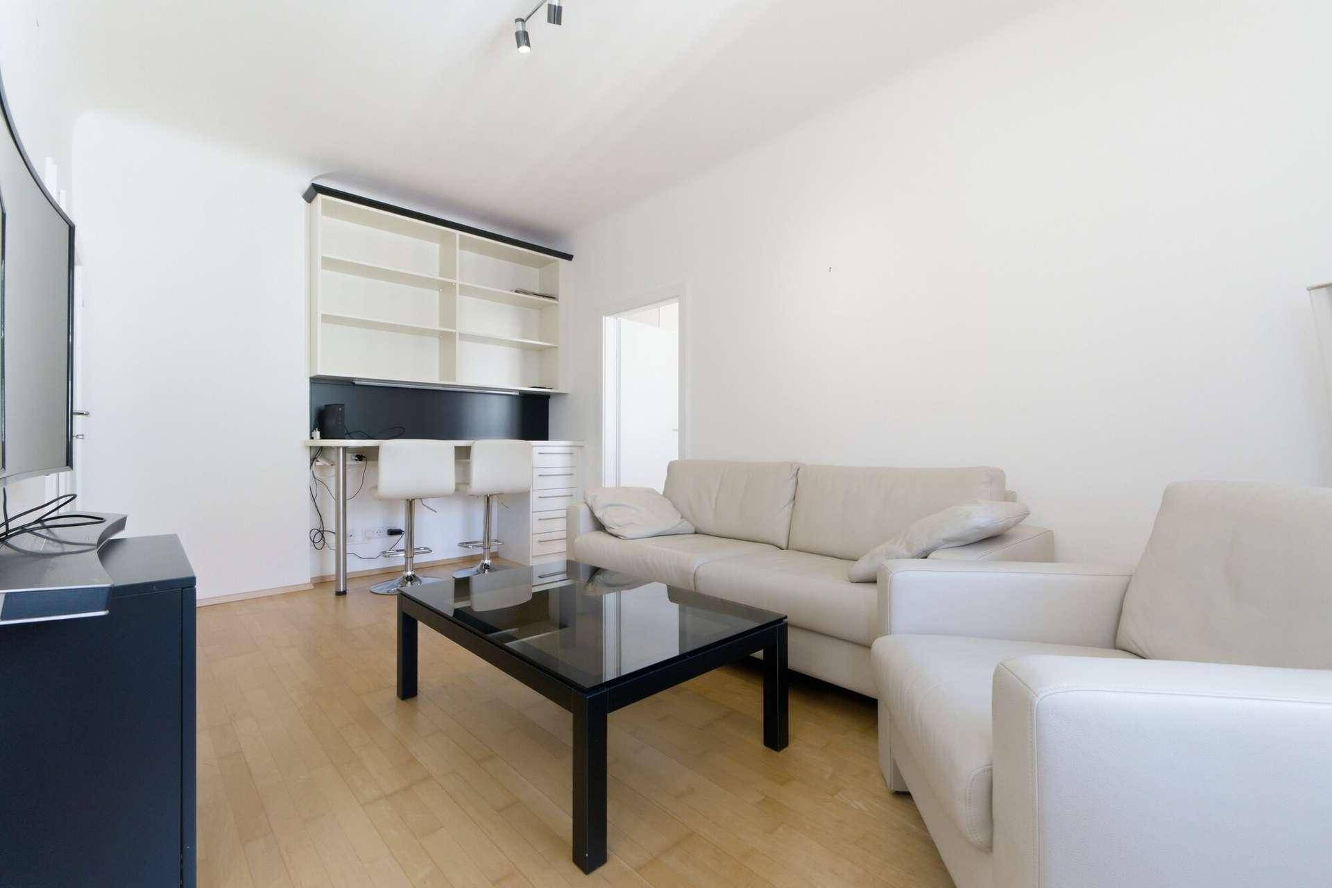 Wohnzimmer mit beigem Sofa, Couchtisch und einem integrierten Regal mit Barhockern.