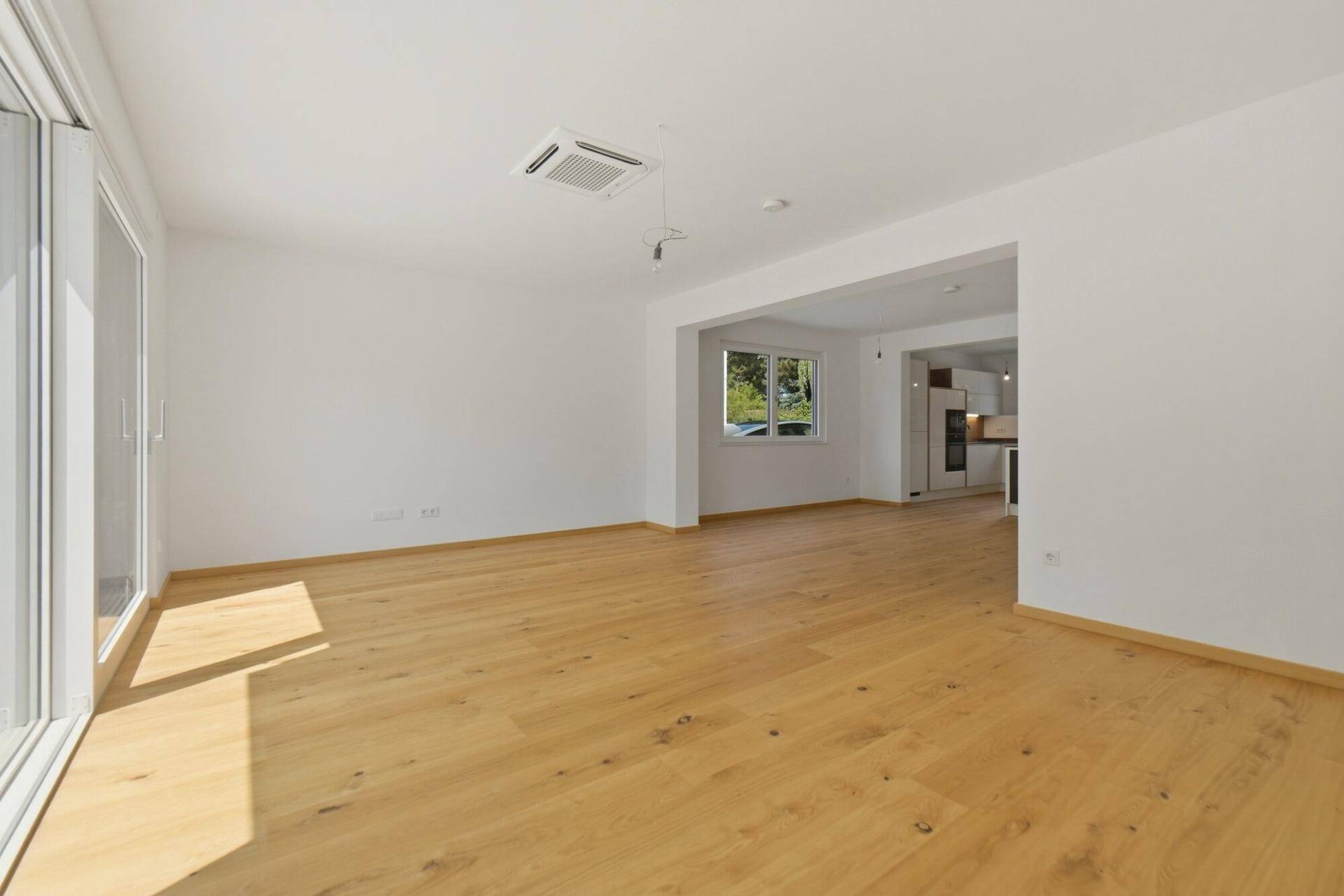 Heller Wohnbereich mit Holzboden, großen Schiebetüren und Blick in die Küche, mit Klimaanlage.