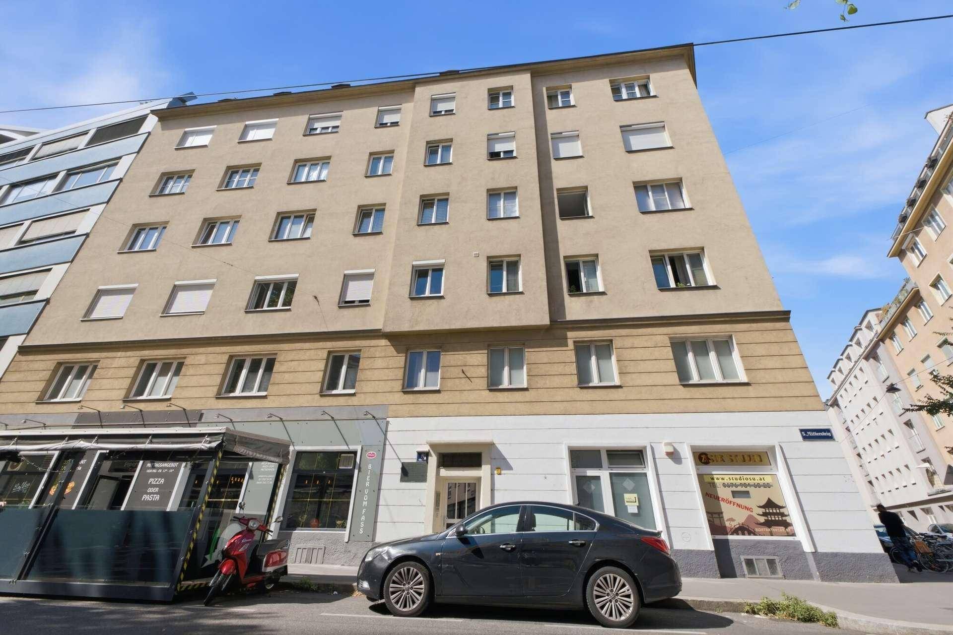 Mehrstöckiges Wohngebäude mit Geschäften im Erdgeschoss und vielen Fenstern.
