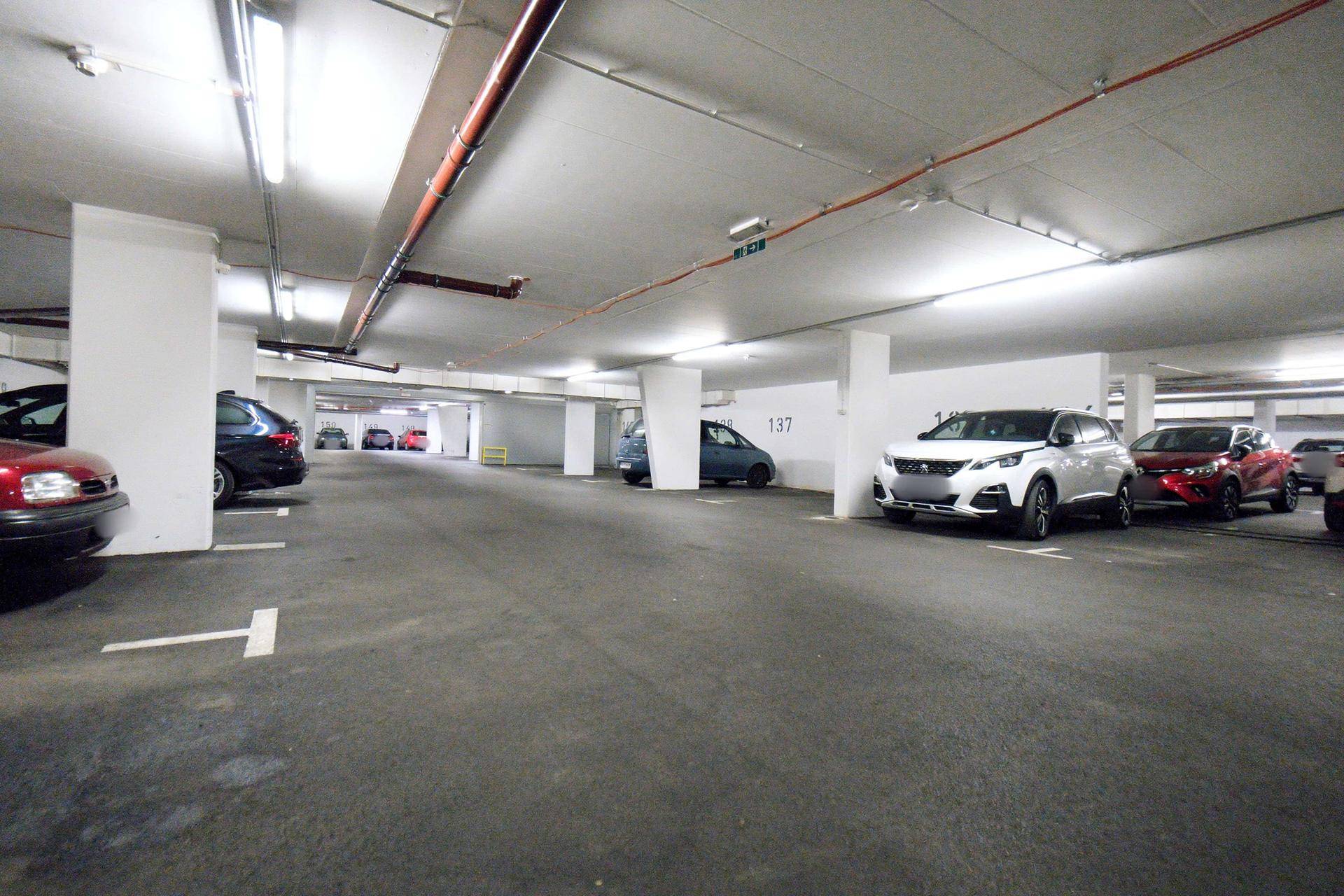 Geräumige Tiefgarage mit vielen Stellplätzen, beleuchtet und mit mehreren geparkten Fahrzeugen.