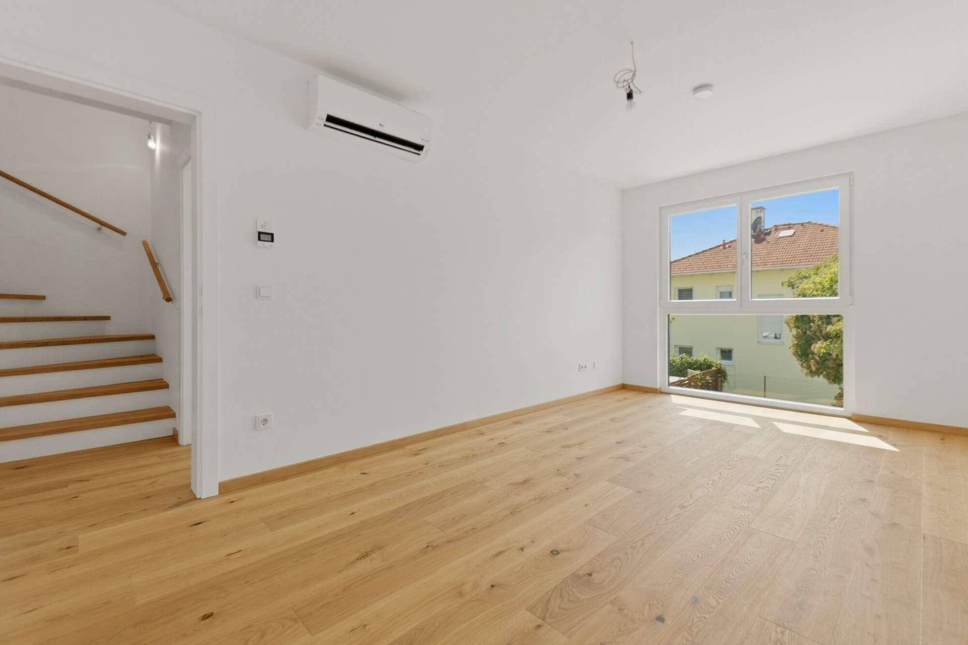 Helles Wohnzimmer mit Holzboden, großen Fenstern und Klimaanlage, bereit zur individuellen Gestaltung.