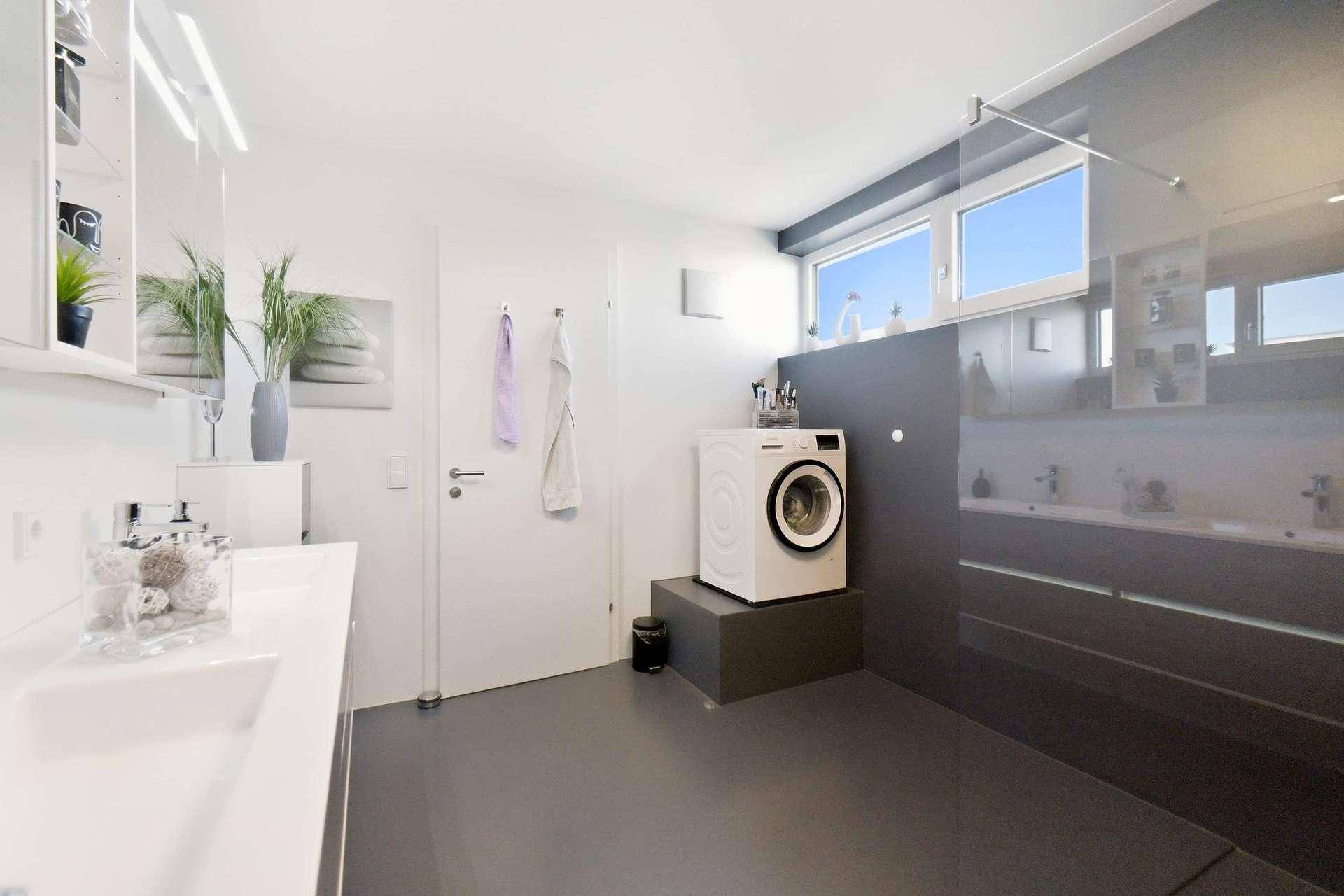 Helles Badezimmer mit Waschmaschine, Doppelwaschbecken und Fenster für natürliche Belüftung.