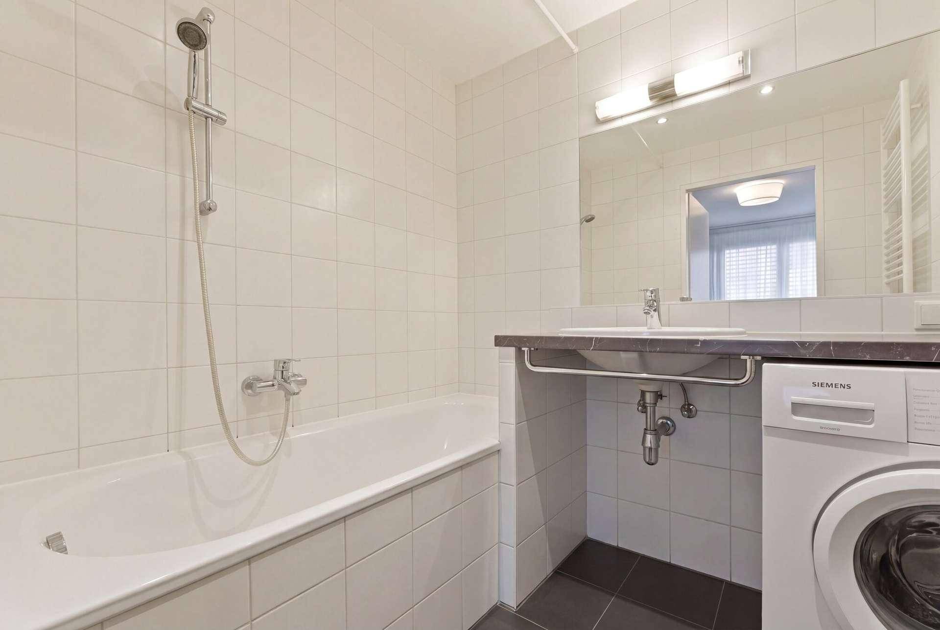 Badezimmer mit Badewanne, Duschfunktion, Waschbecken und integrierter Waschmaschine.
