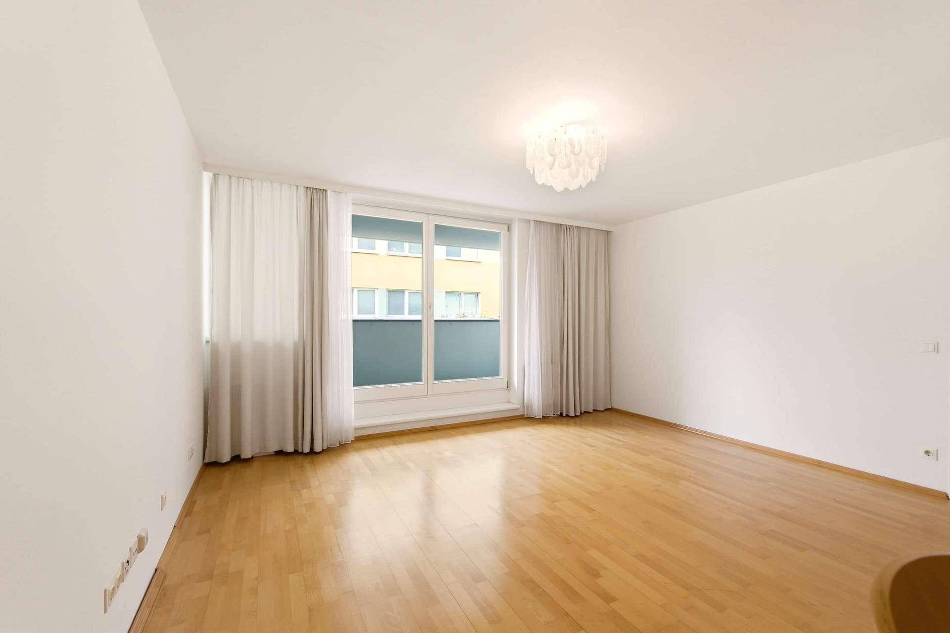Geräumiges Wohnzimmer mit hellem Parkettboden und großem Fenster mit Blick nach draußen.