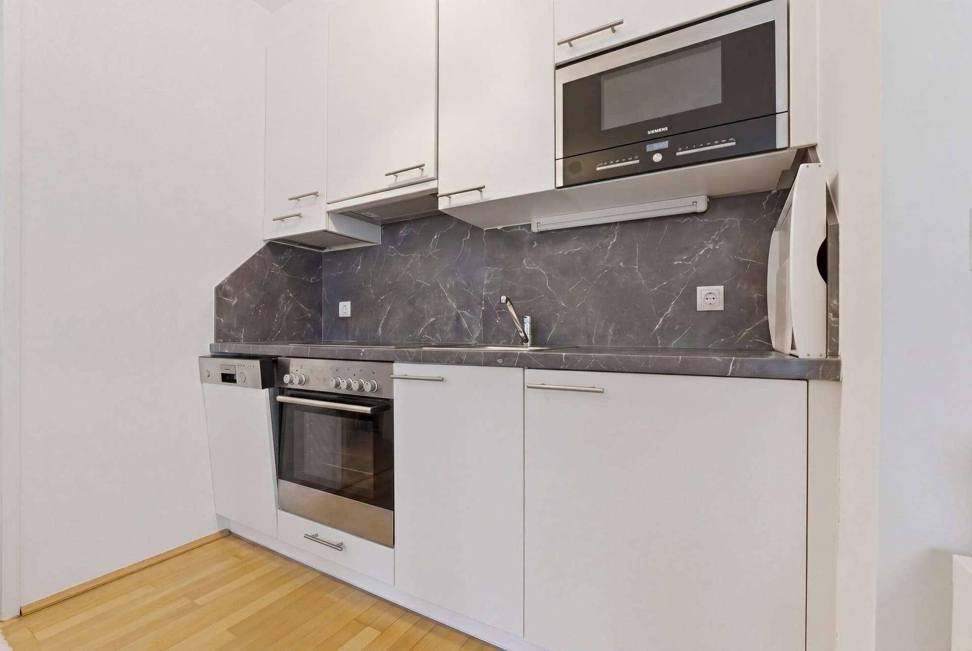 Moderne Einbauküche mit weißen Schränken, Mikrowelle, Backofen und Geschirrspüler.