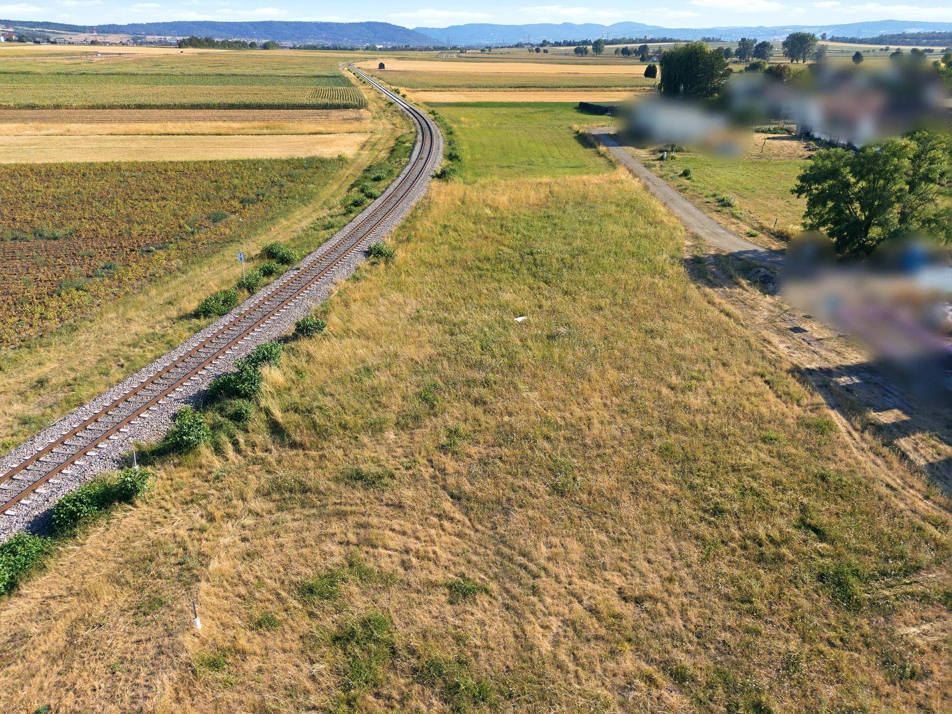 Luftaufnahme eines weiten Feldes mit Bahngleisen und verschwommenen Gebäuden in der ländlichen Umgebung.