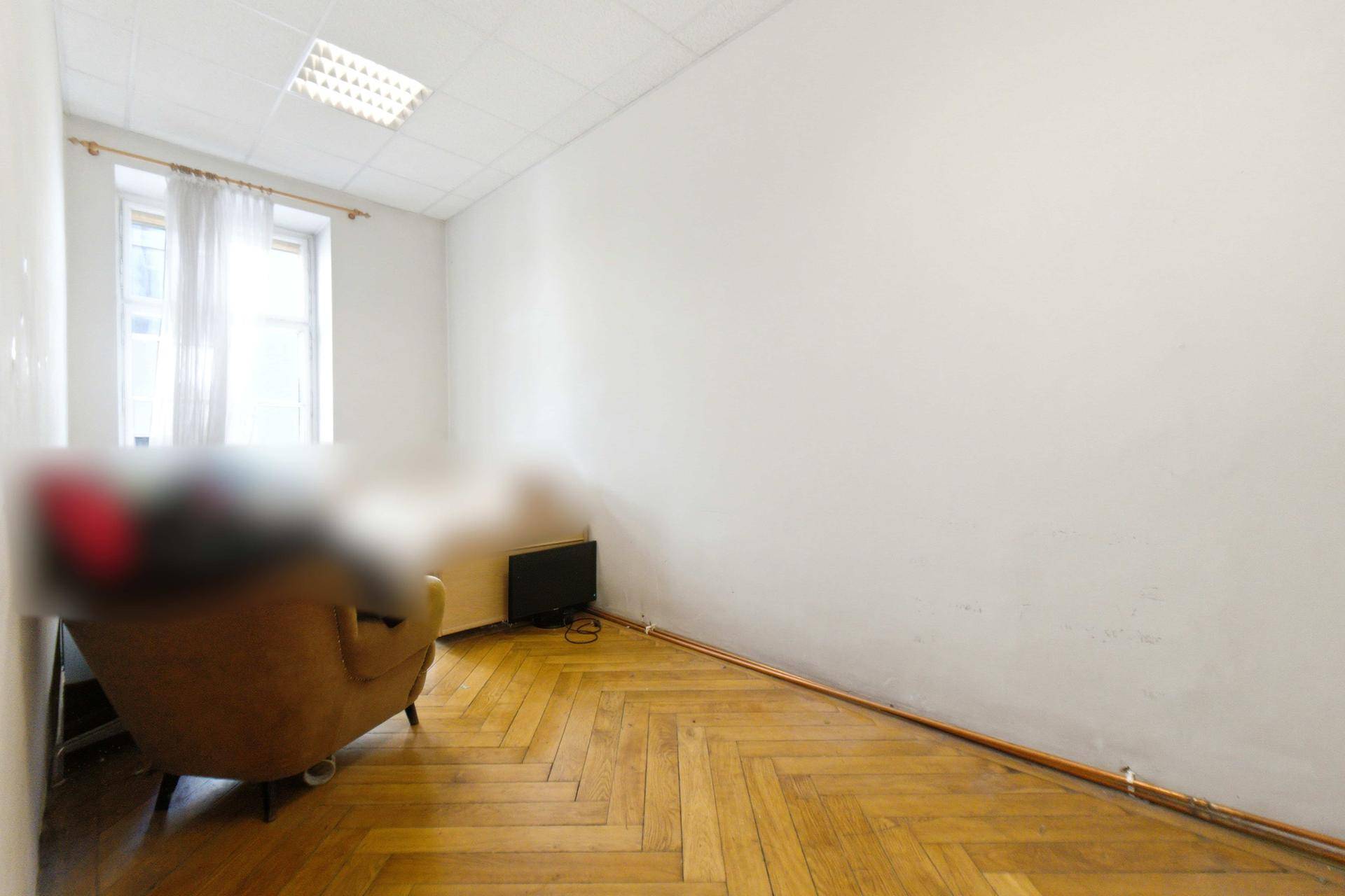 Gemütlicher Raum mit Fischgrätparkett und einem Fenster, möbliert mit einem Sessel und Fernseher.