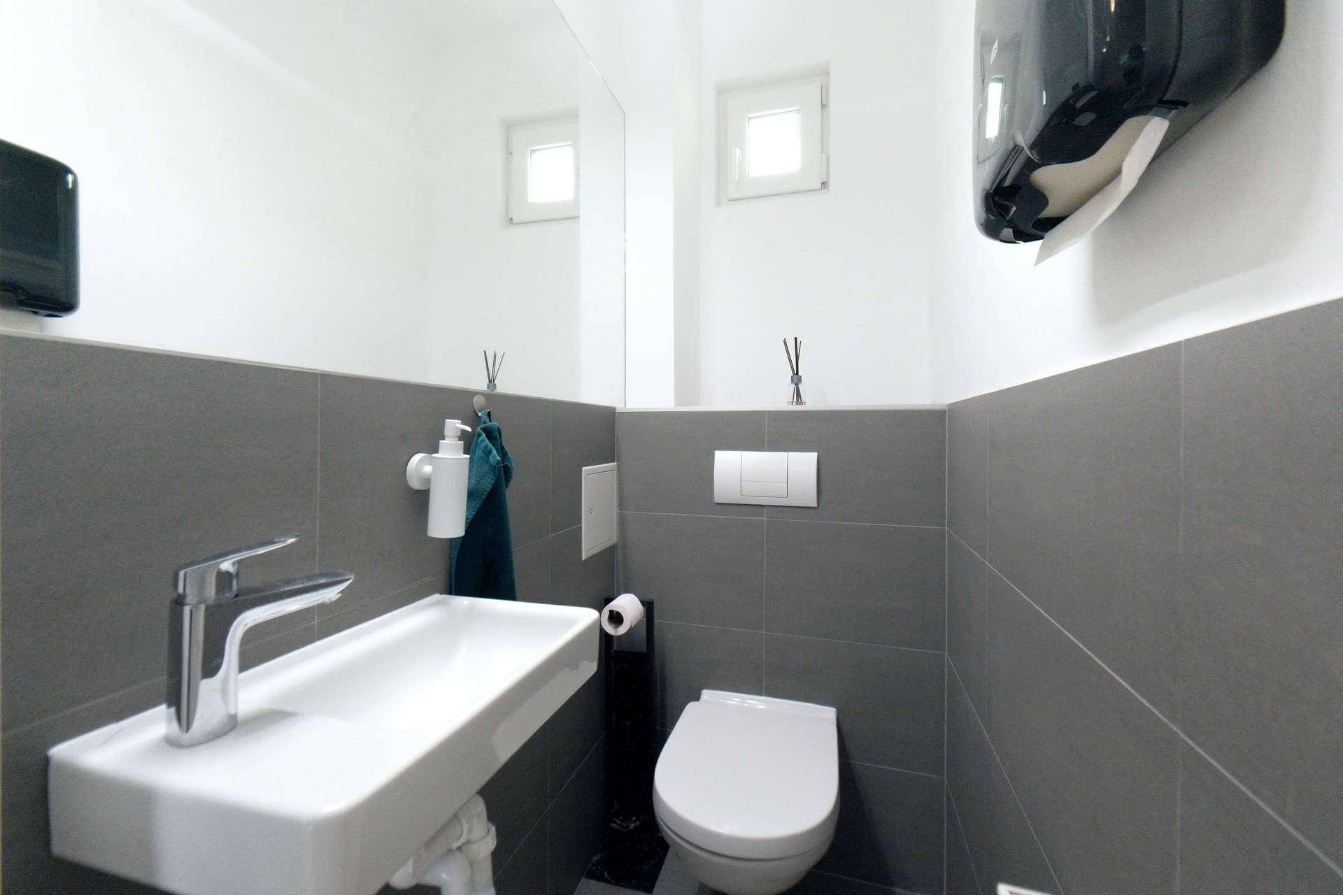 Modernes Gäste-WC mit kleinem Waschbecken, Wand-WC und grauen Fliesen.