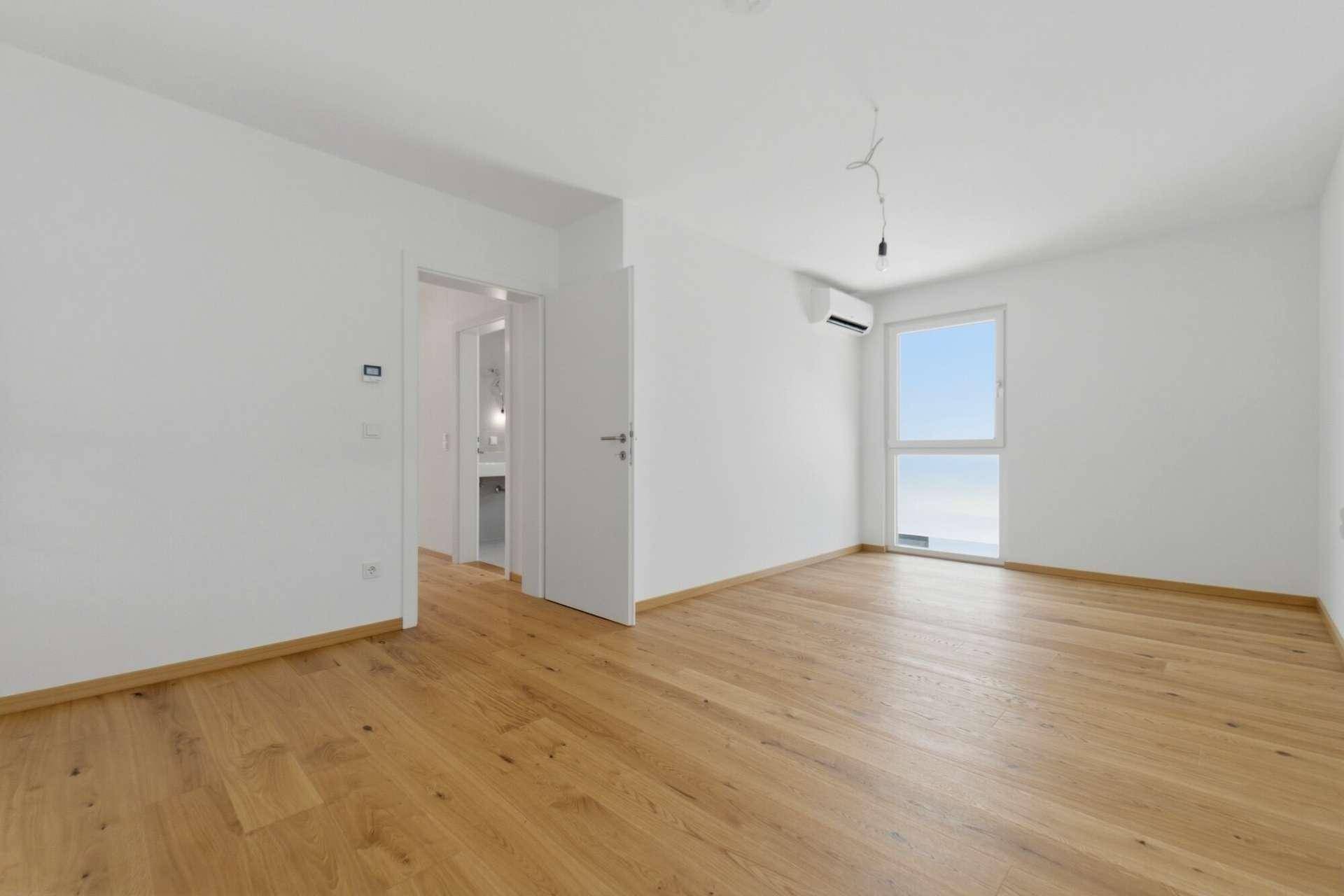 Geräumiges Schlafzimmer mit Holzboden, Klimaanlage und Zugang zu einem modernen Badezimmer.