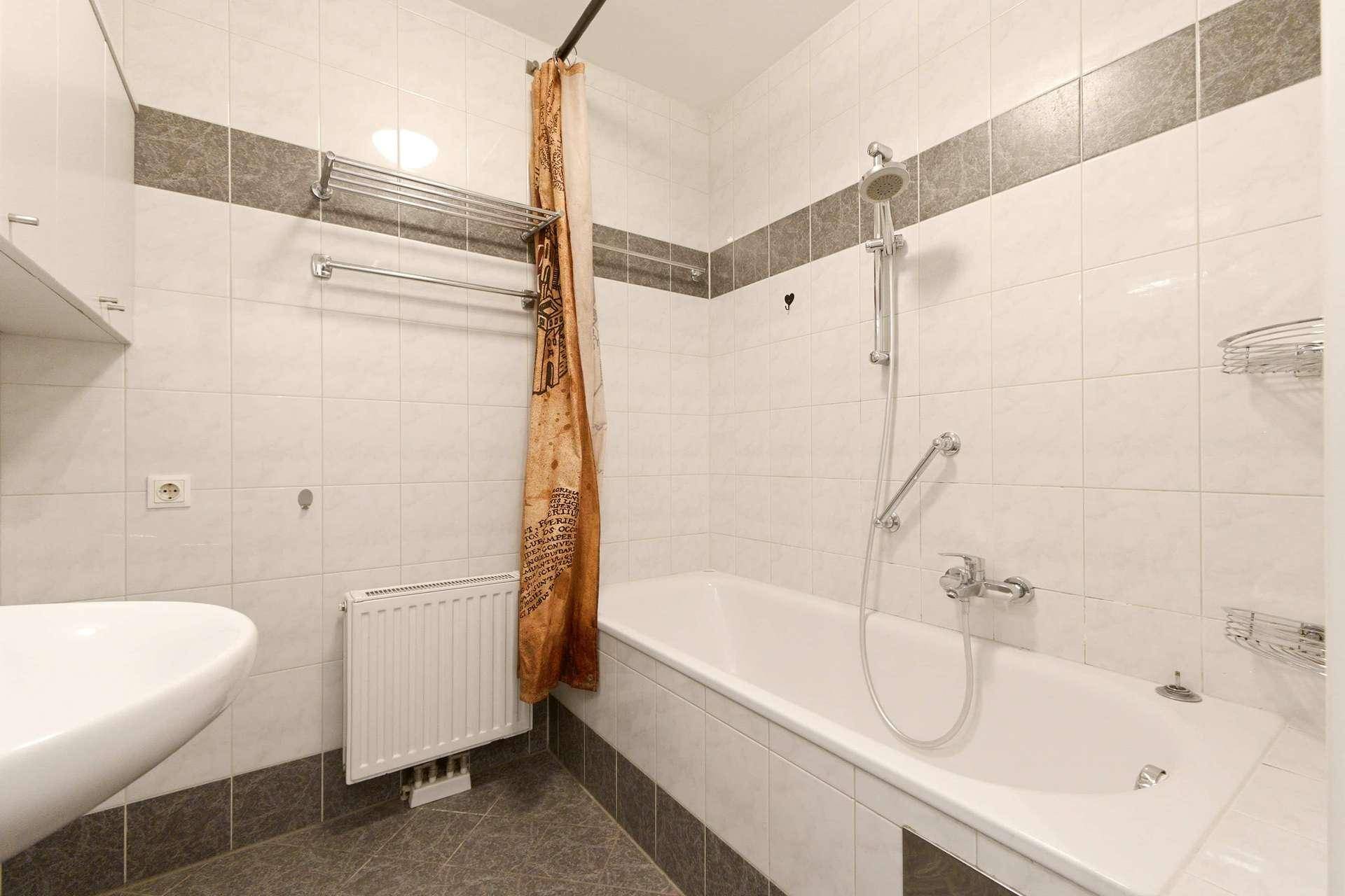 Badezimmer mit Badewanne, Duschvorhang, Waschbecken und gefliesten Wänden und Boden.