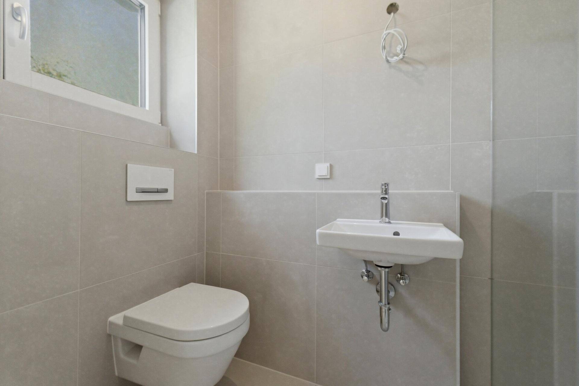 Kompaktes WC mit Waschbecken, Hänge-WC und Fenster, ideal für Gäste.