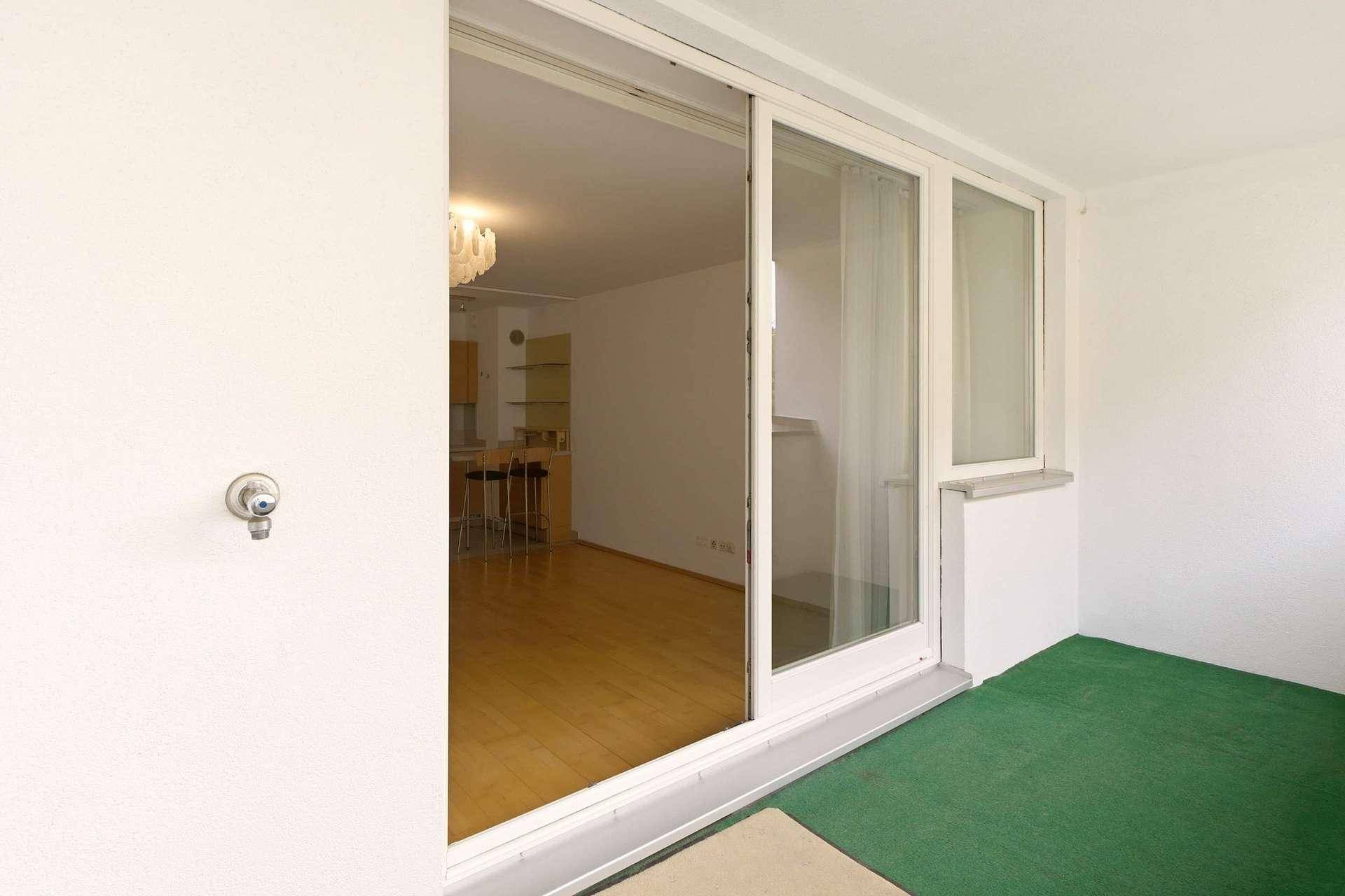 Balkon mit grünem Bodenbelag und großer Schiebetür, die zum Innenbereich der Wohnung führt.