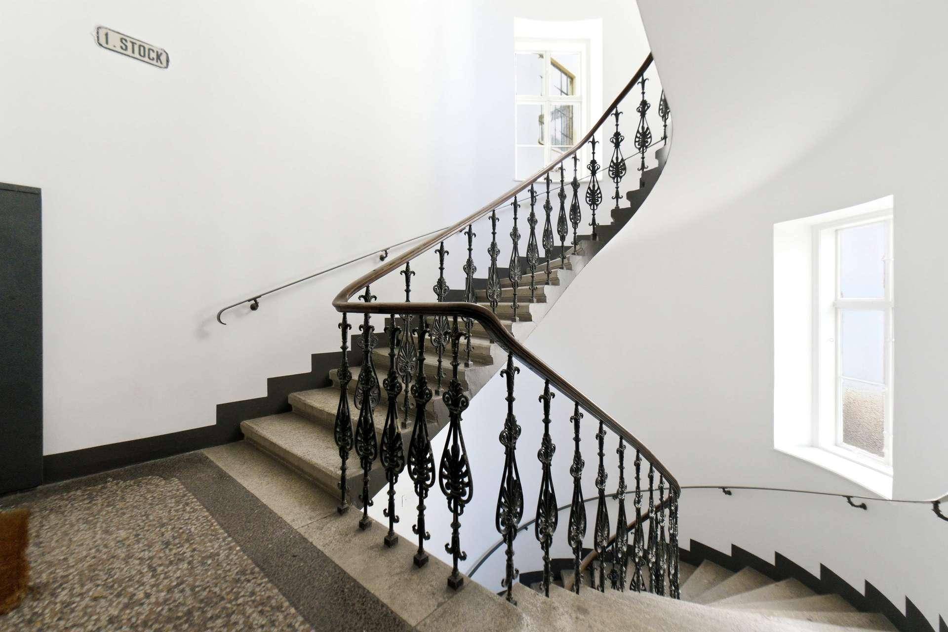 Elegantes Treppenhaus mit geschwungener Form, schmiedeeisernem Geländer und viel Tageslicht.