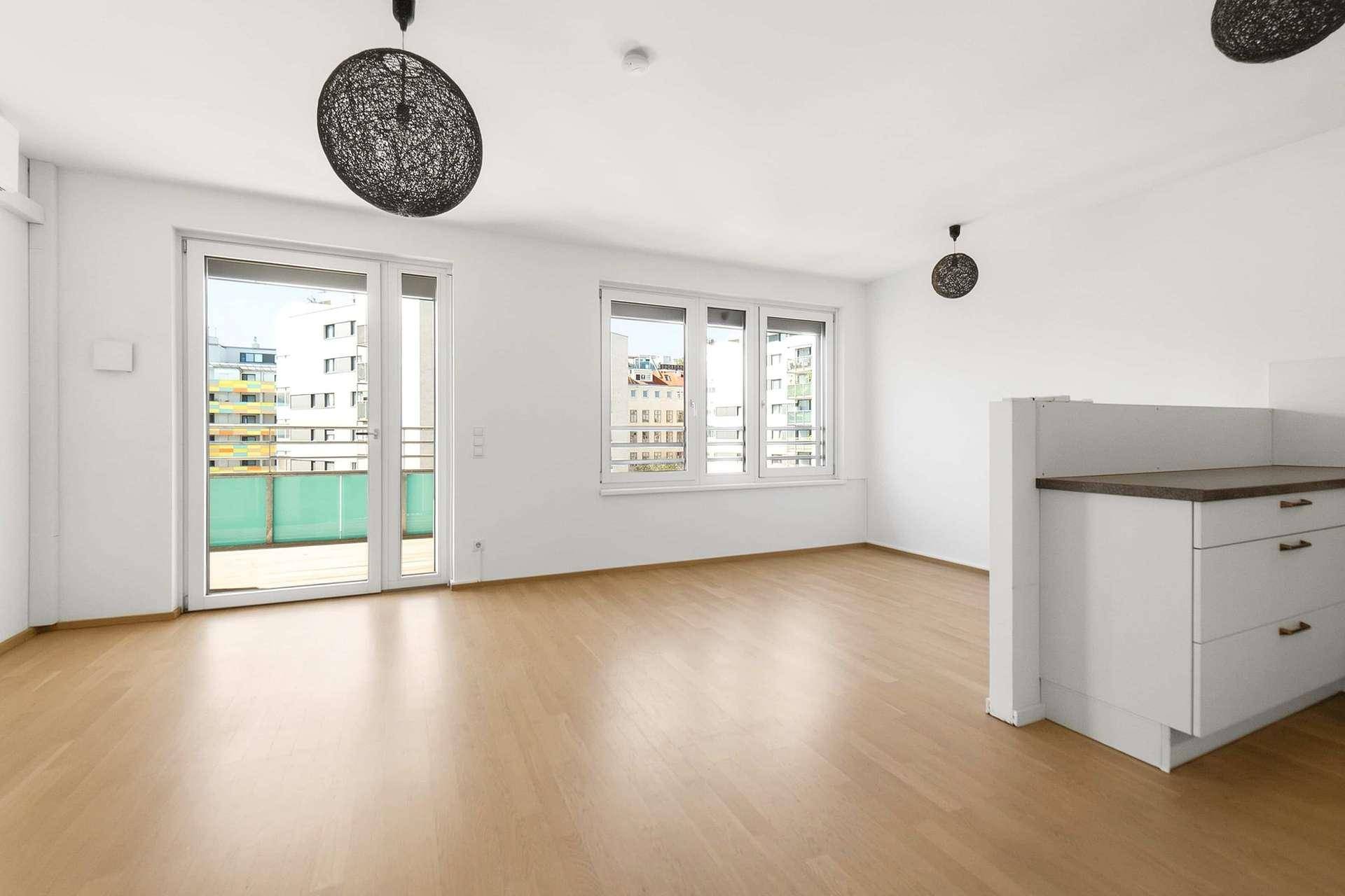 Offener Wohnbereich mit Küchenzeile, Holzboden und Zugang zum Balkon.