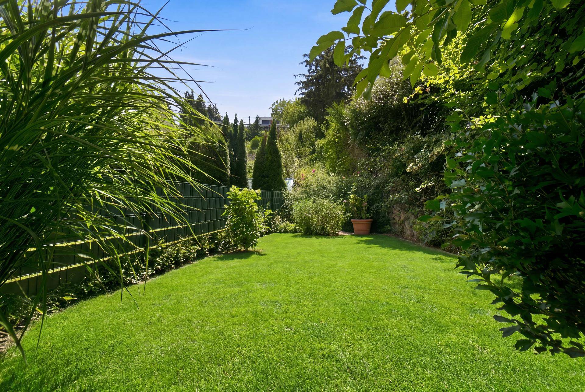 Virtuell inszenierter Gartenbereich mit gepflegtem Rasen und üppiger Bepflanzung, sonnig und einladend.