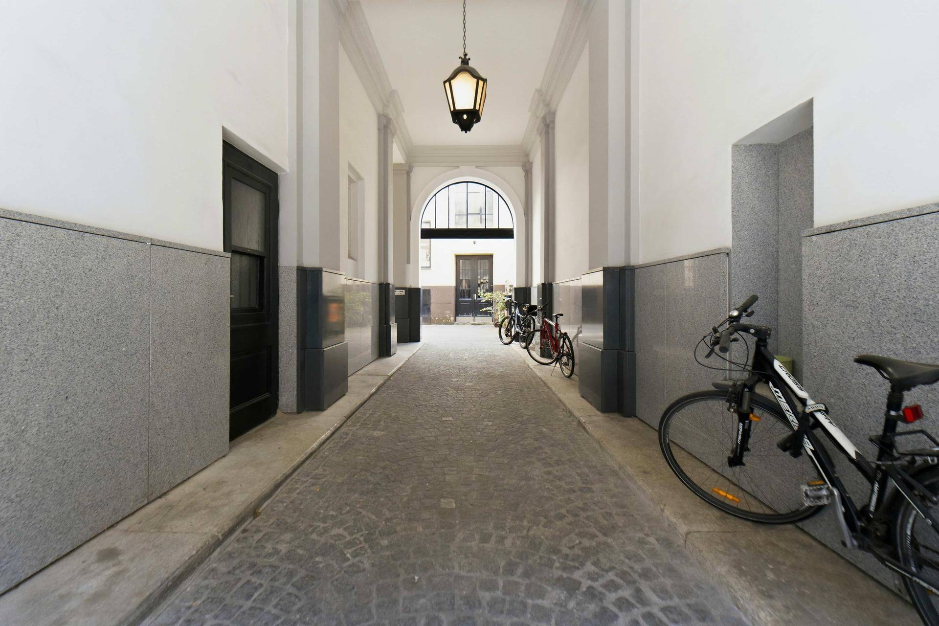 Überdachter Durchgang zu einem Innenhof mit Kopfsteinpflaster und abgestellten Fahrrädern.