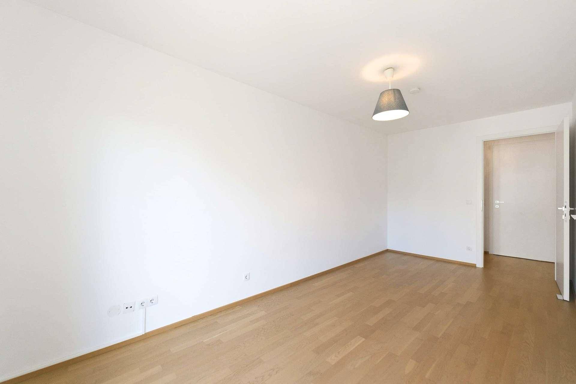 Leerer Raum mit hellem Holzboden und Zugang zu einem weiteren Bereich.