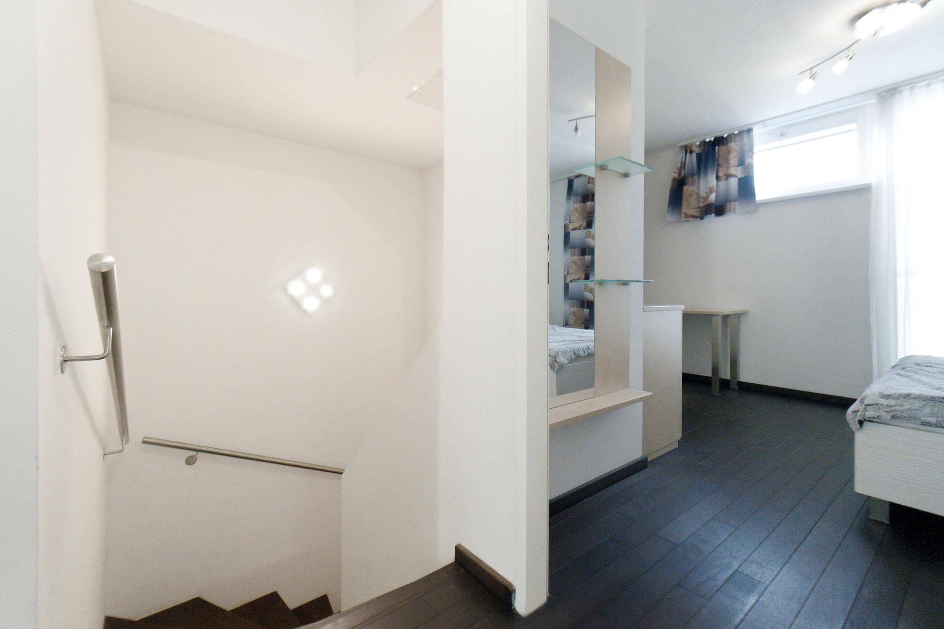 Flur mit Treppenabgang und Spiegel, führt zu einem weiteren Schlafzimmer.