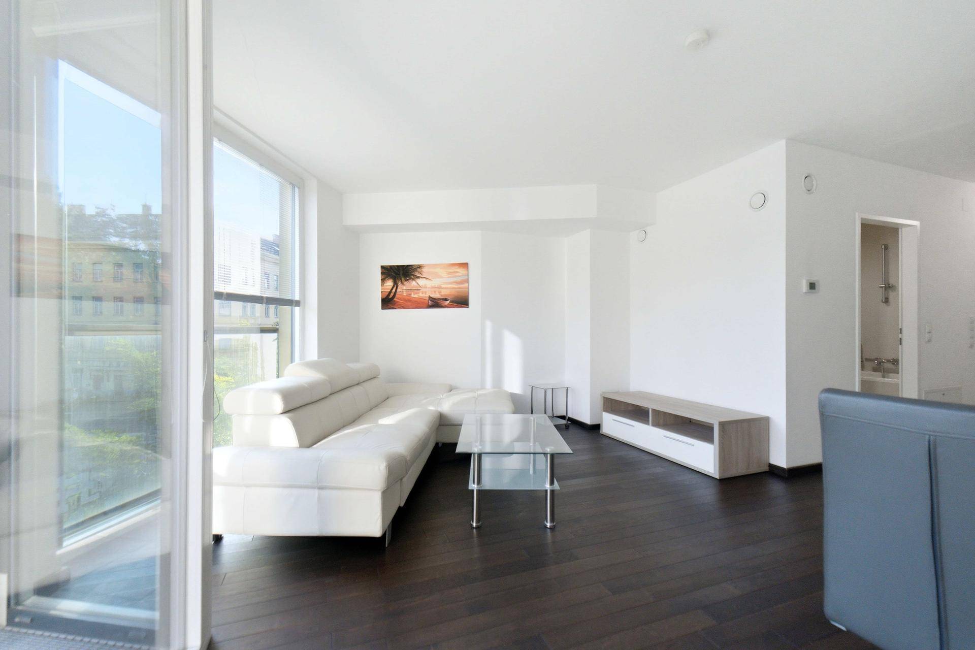 Heller Wohnbereich mit weißem Ecksofa, dunklem Holzboden und großen Fenstern mit Stadtblick.