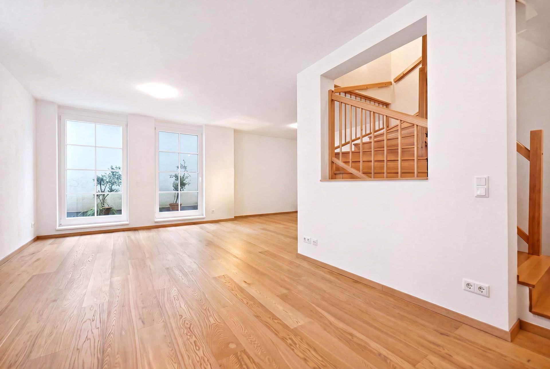 Geräumiger, heller Wohnbereich mit Holzboden und offener Holztreppe, bereit für individuelle Einrichtung.