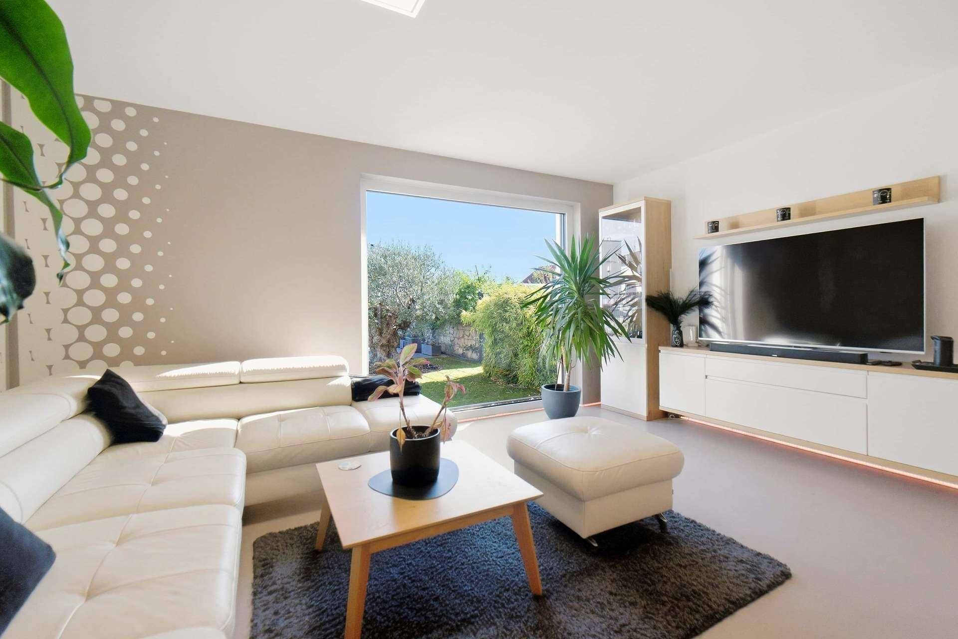 Modern eingerichtetes Wohnzimmer mit großem Fernseher, weißem Sofa und Blick in den Garten.